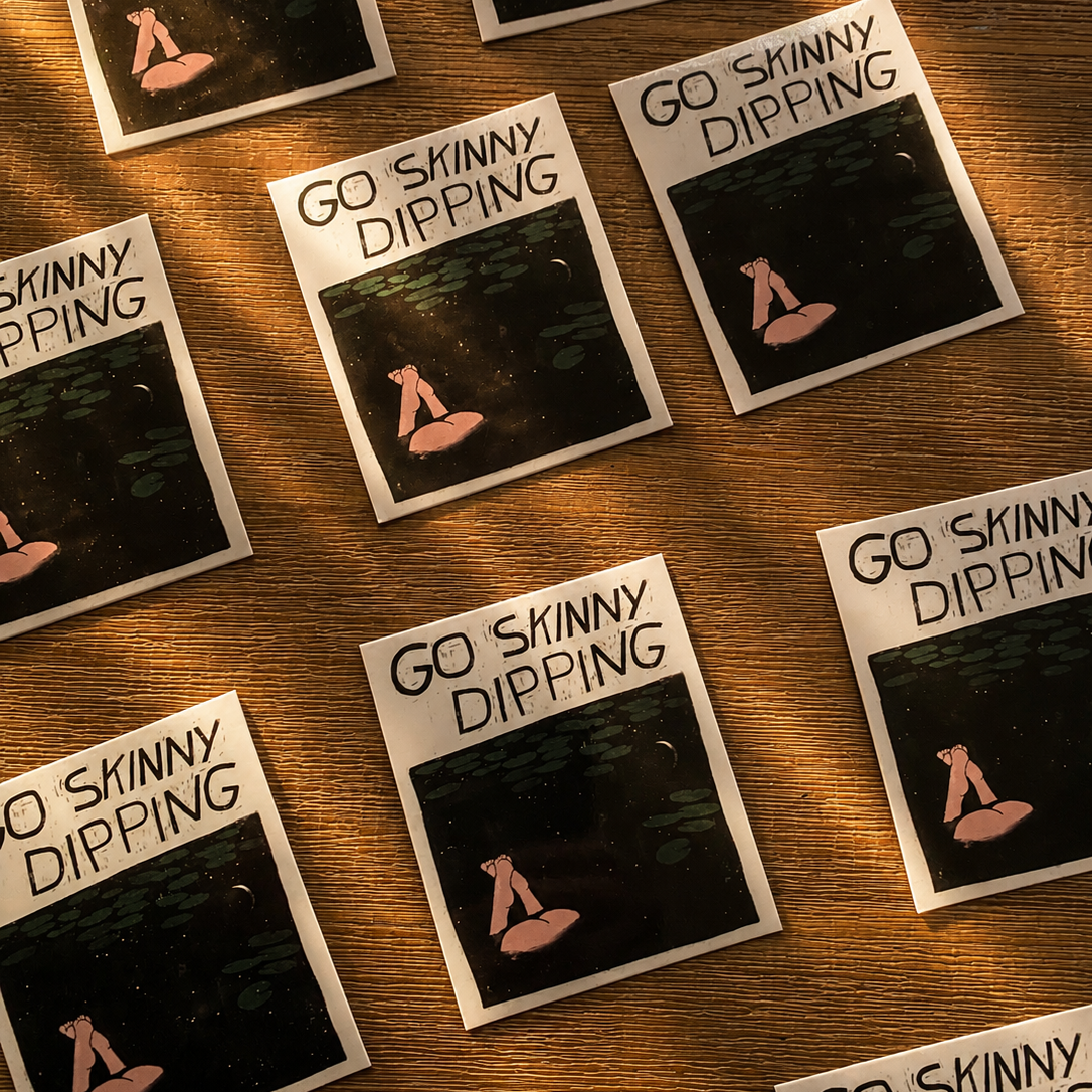 Multiple 'Go Skinny Dipping' stickers on a wooden surface