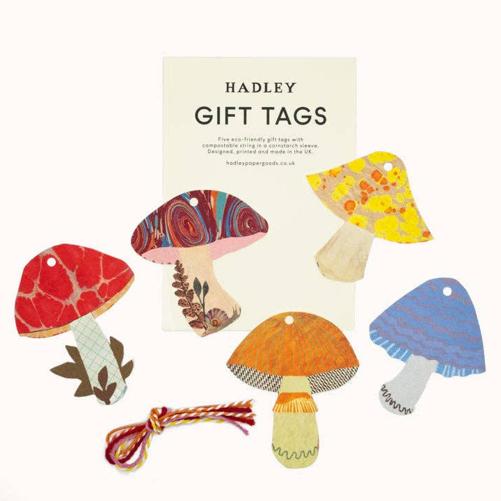 A set of Hadley gift tags featuring whimsical mushroom illustrations in red, orange, yellow, blue, and patterned designs, with a cream card reading 'HADLEY GIFT TAGS' behind them on a white background.