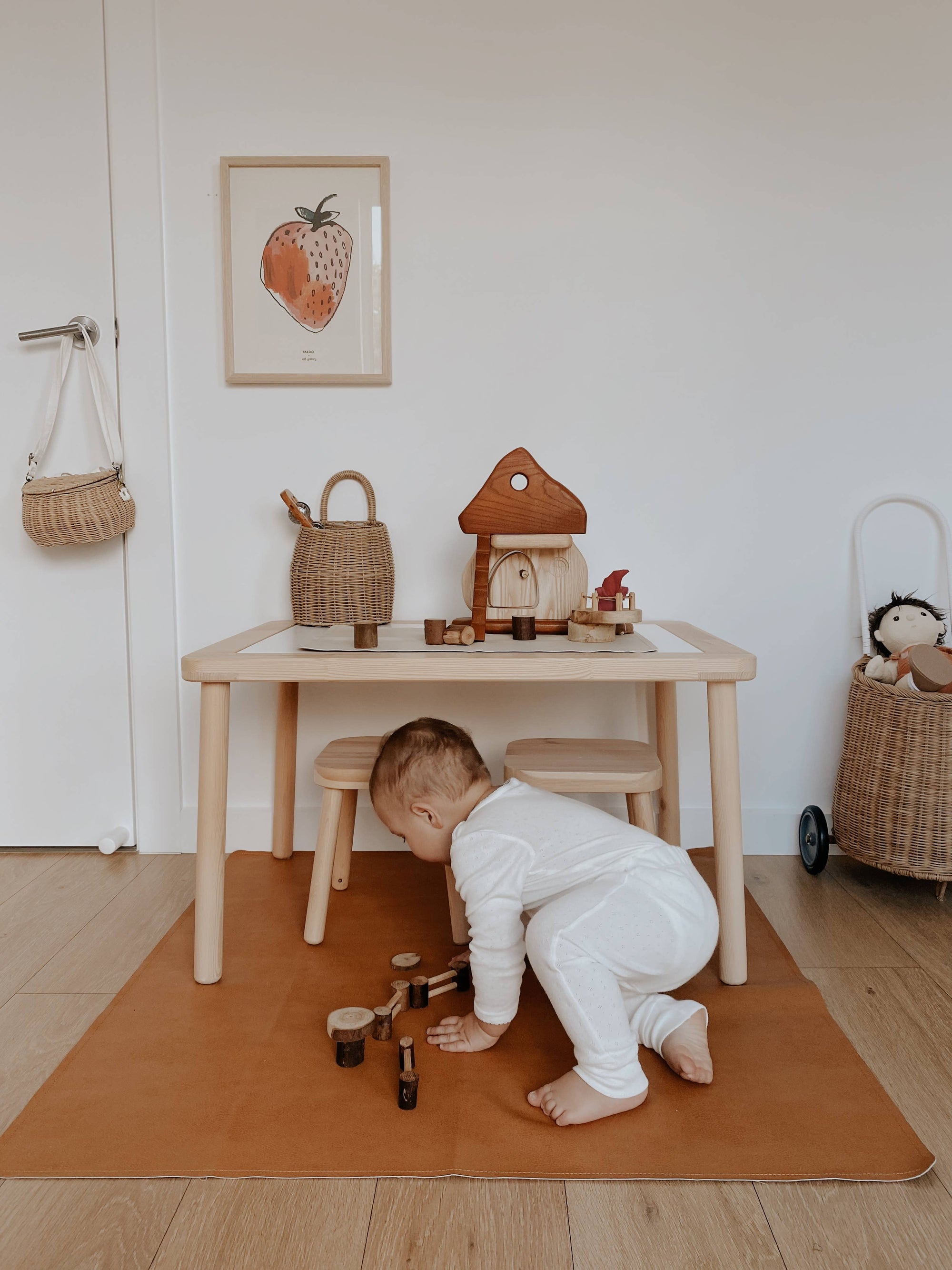 Child playing with toys on a wooden floor in a room with a small table and stools.