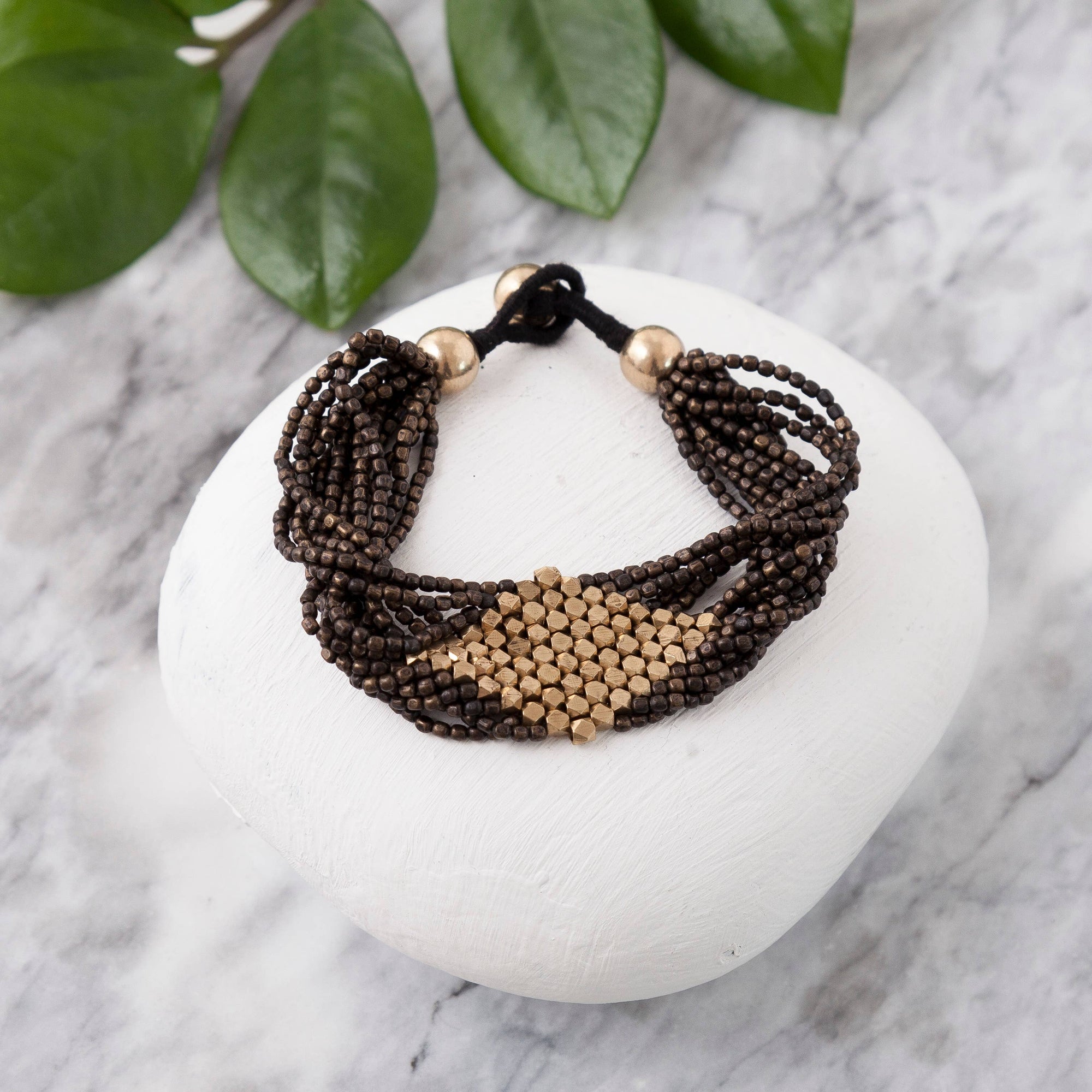 Multistrand beaded bracelet with gold accents on a white stone surface with green leaves.