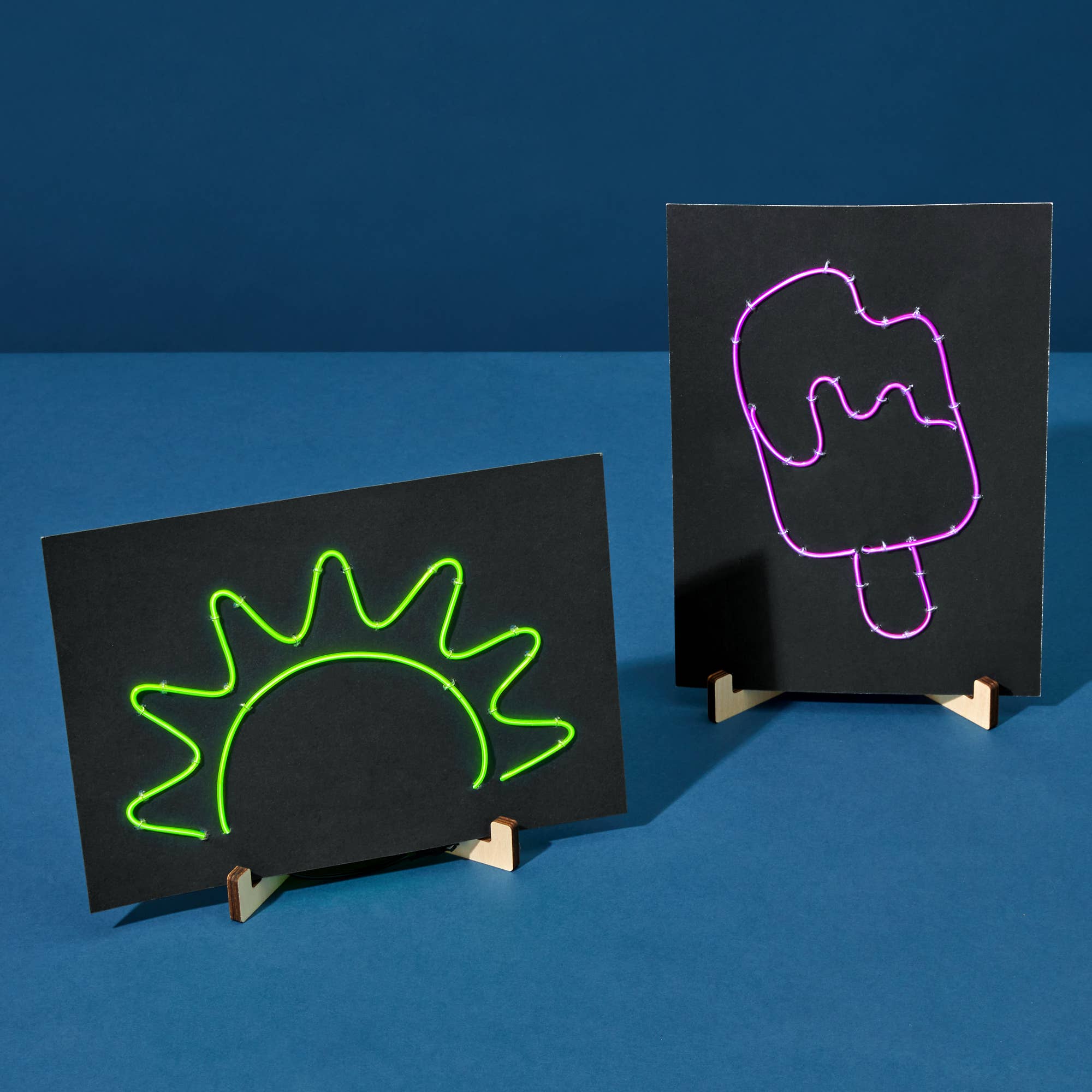 Two black boards with neon drawings of a sun and a popsicle on a blue background