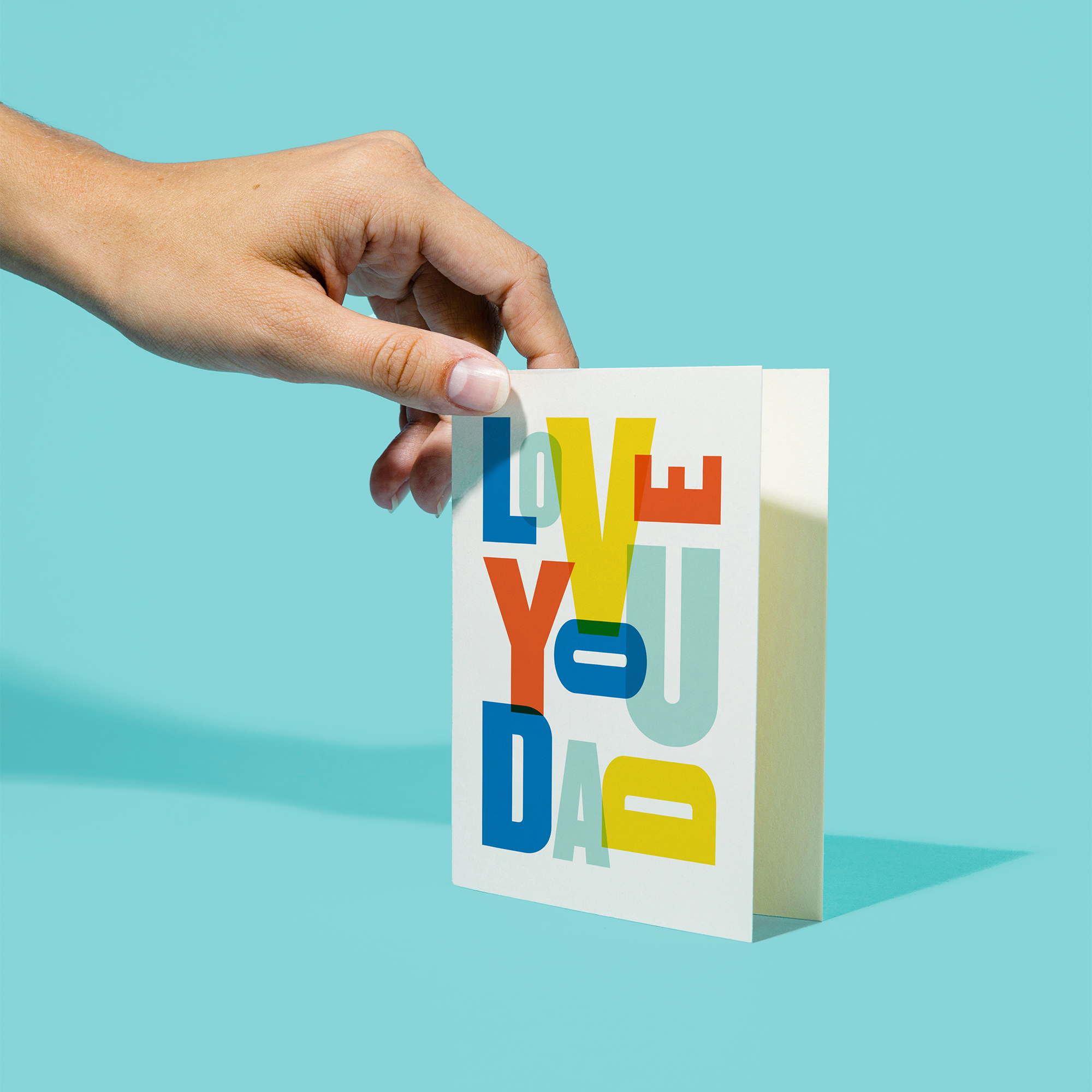 Hand holding a colorful 'I love you dad' card against a blue background