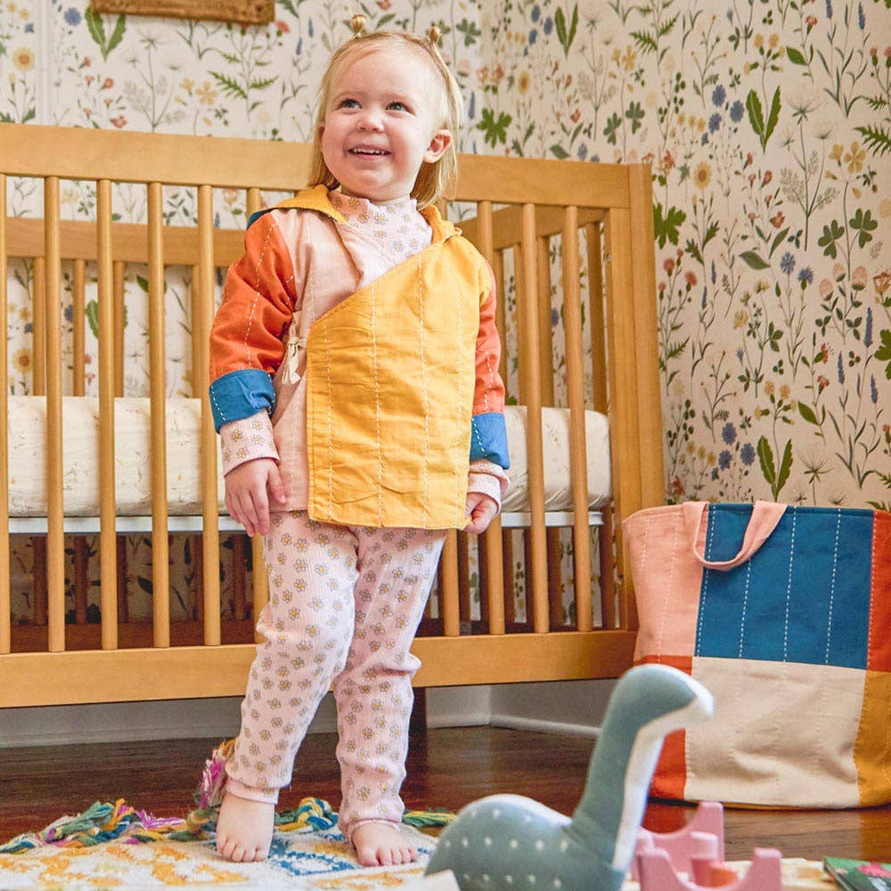 Child standing in a nursery with floral wallpaper and wooden crib