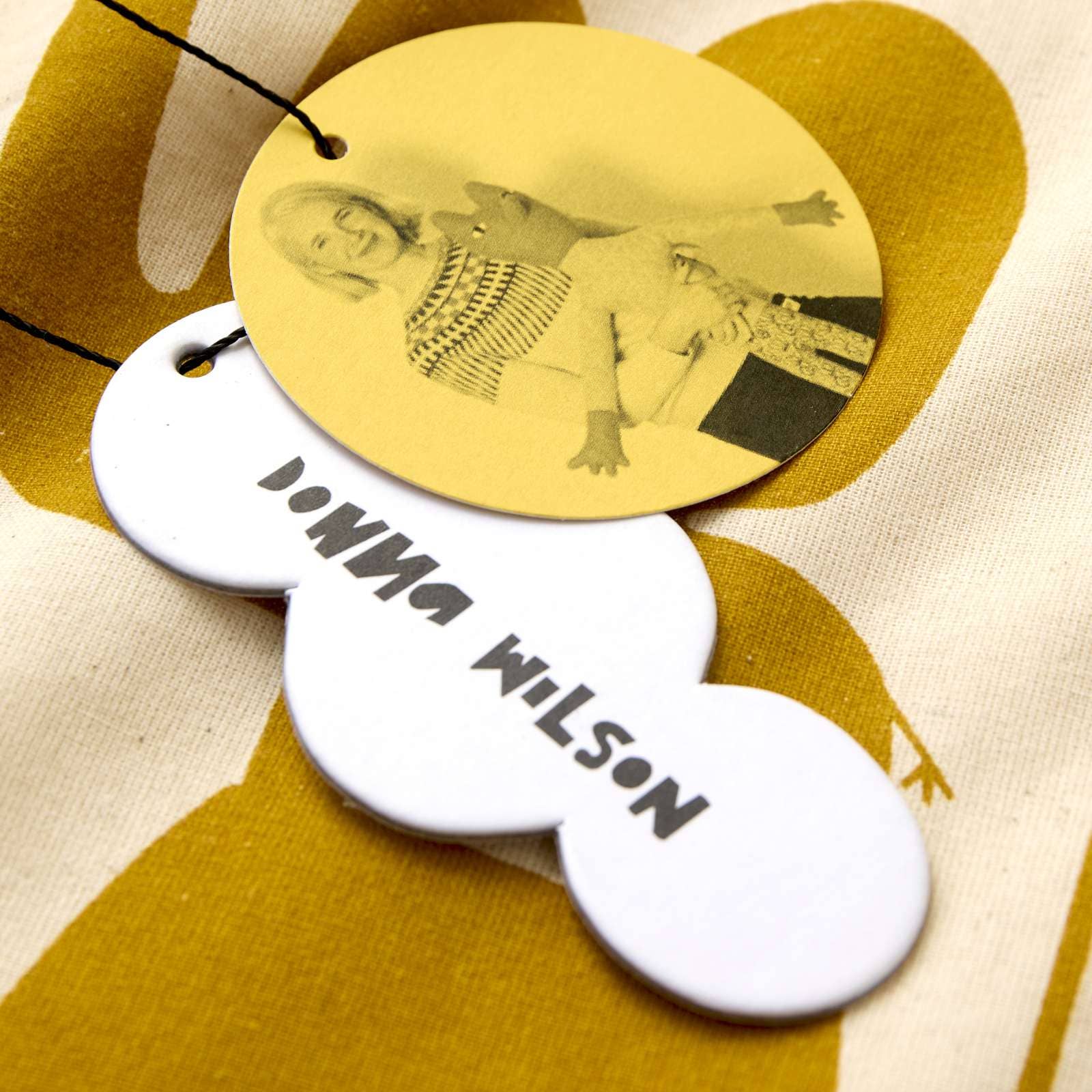 Gold tag with black and white illustration and 'Donna Wilson' text on a yellow and beige background