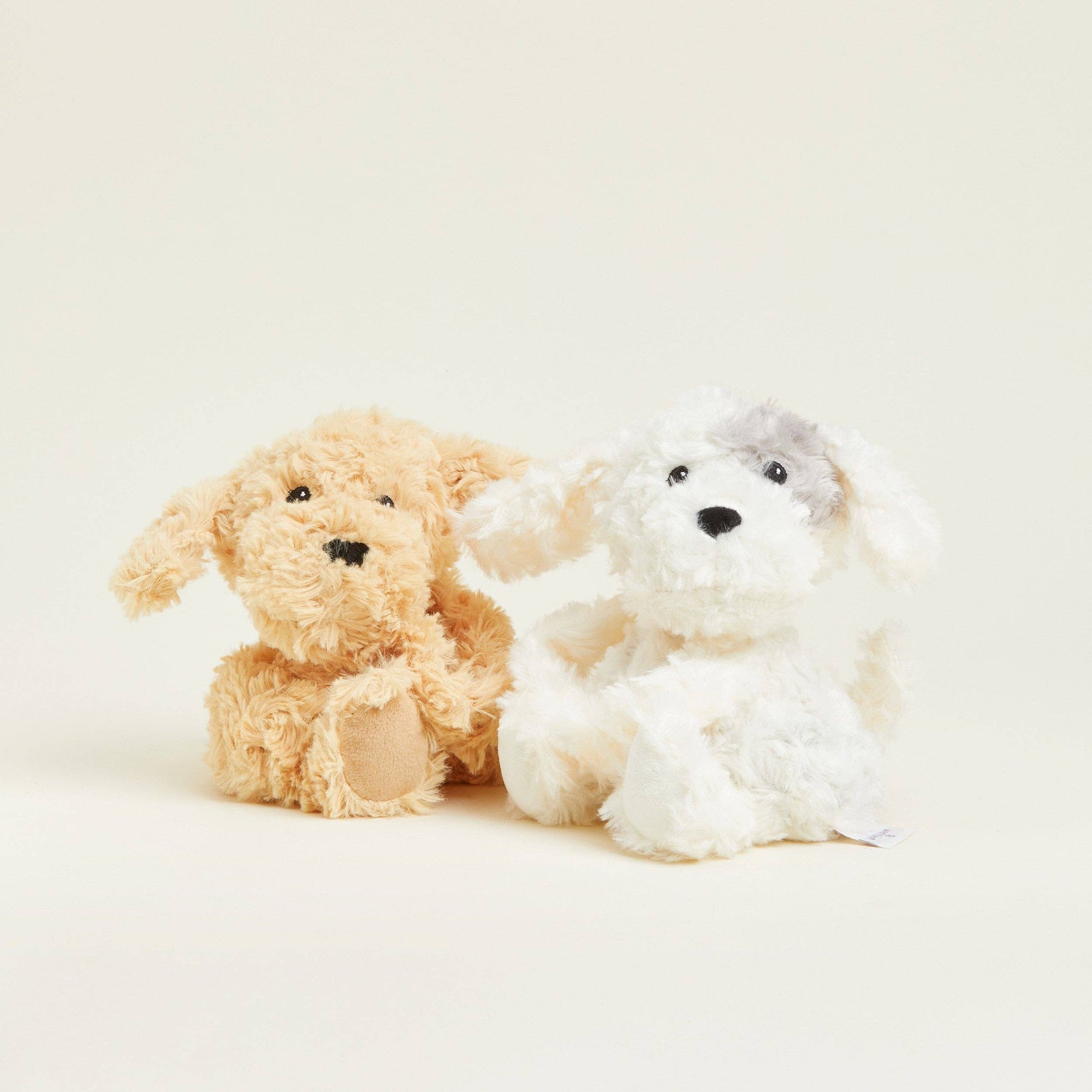 Two plush toys, one brown and one white, sitting side by side on a light background.