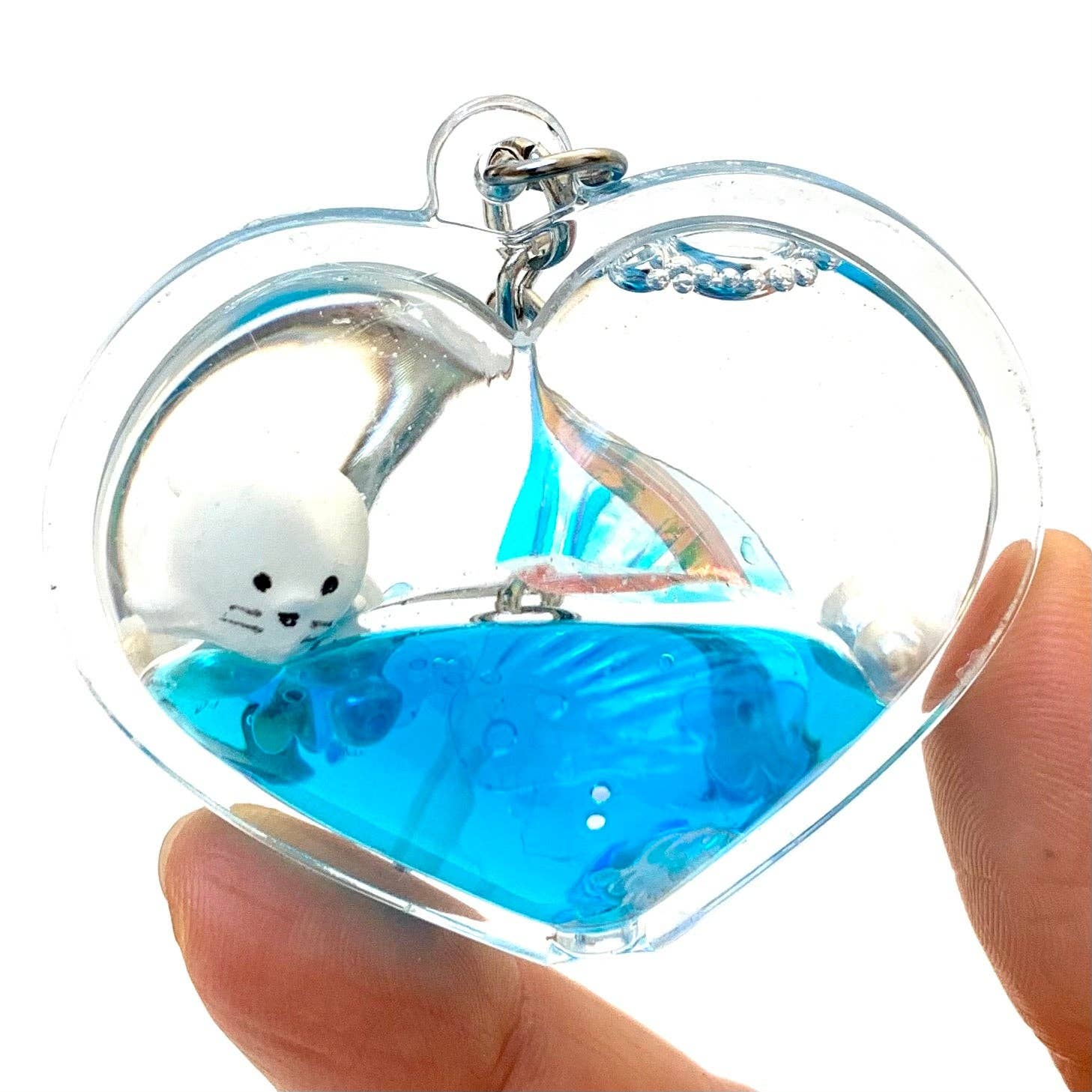 Heart-shaped clear container with blue liquid and a small white creature, held by a hand.