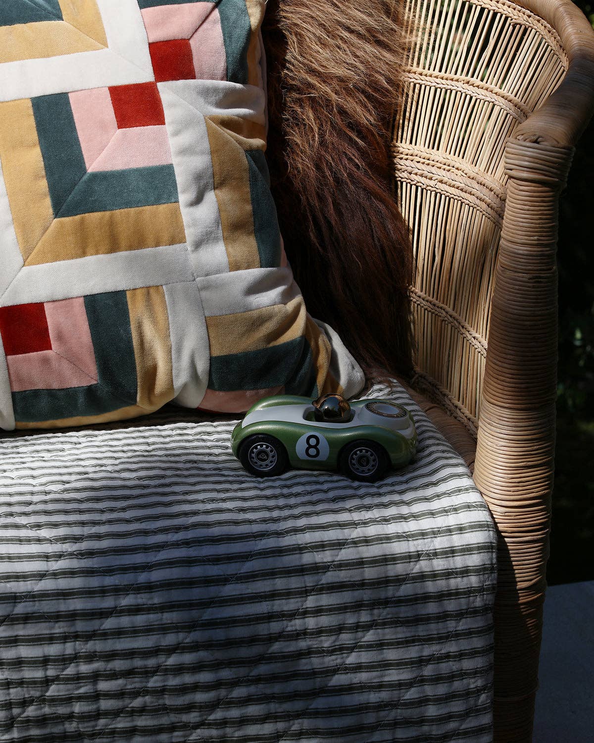Toy car on a striped surface with a patterned pillow and wicker chair in the background