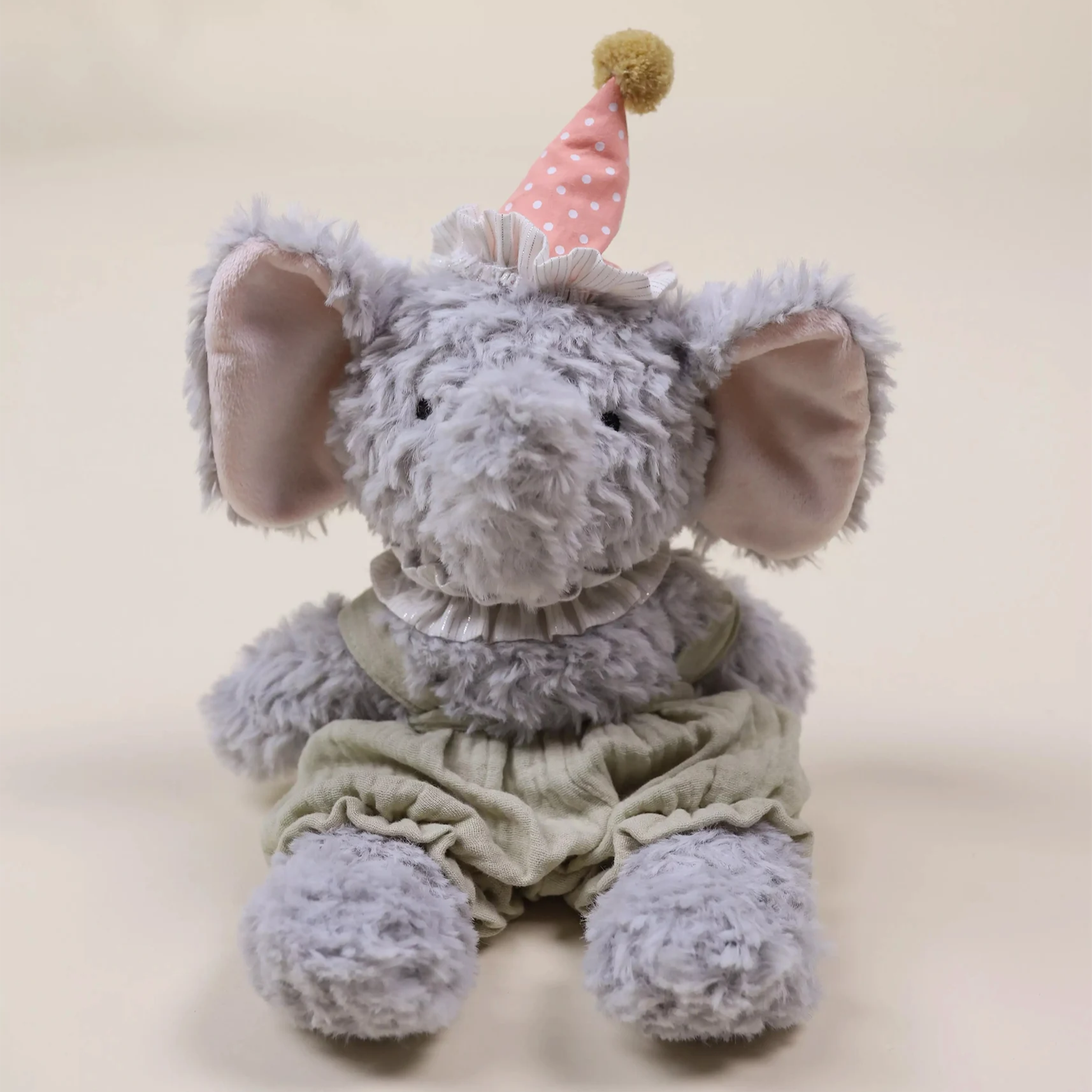 Plush elephant toy wearing a party hat on a beige background