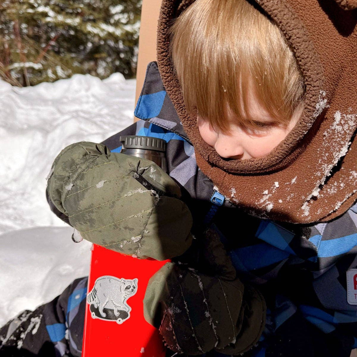 Child in winter clothing with a red snow shovel in a snowy outdoor setting