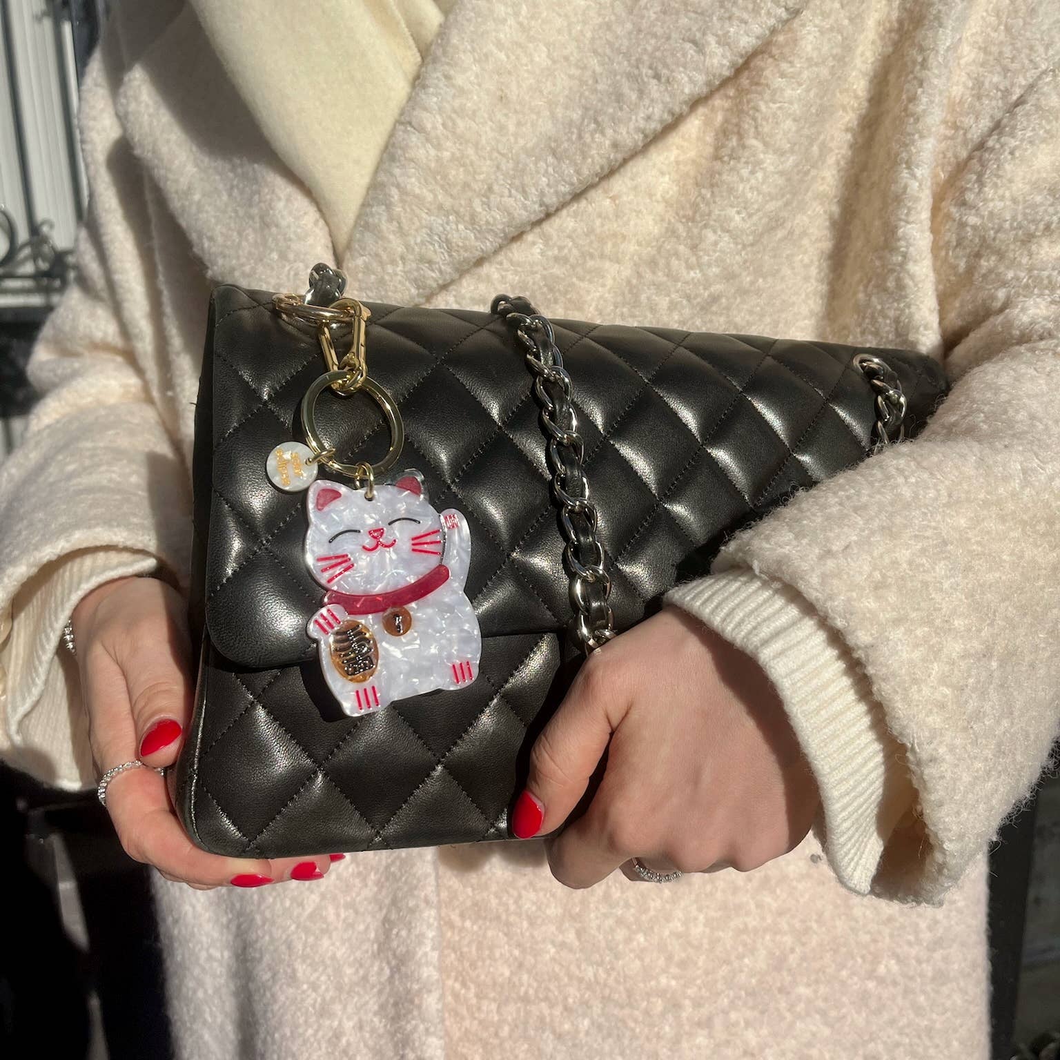Person holding a black quilted handbag with a decorative charm, wearing a beige coat.