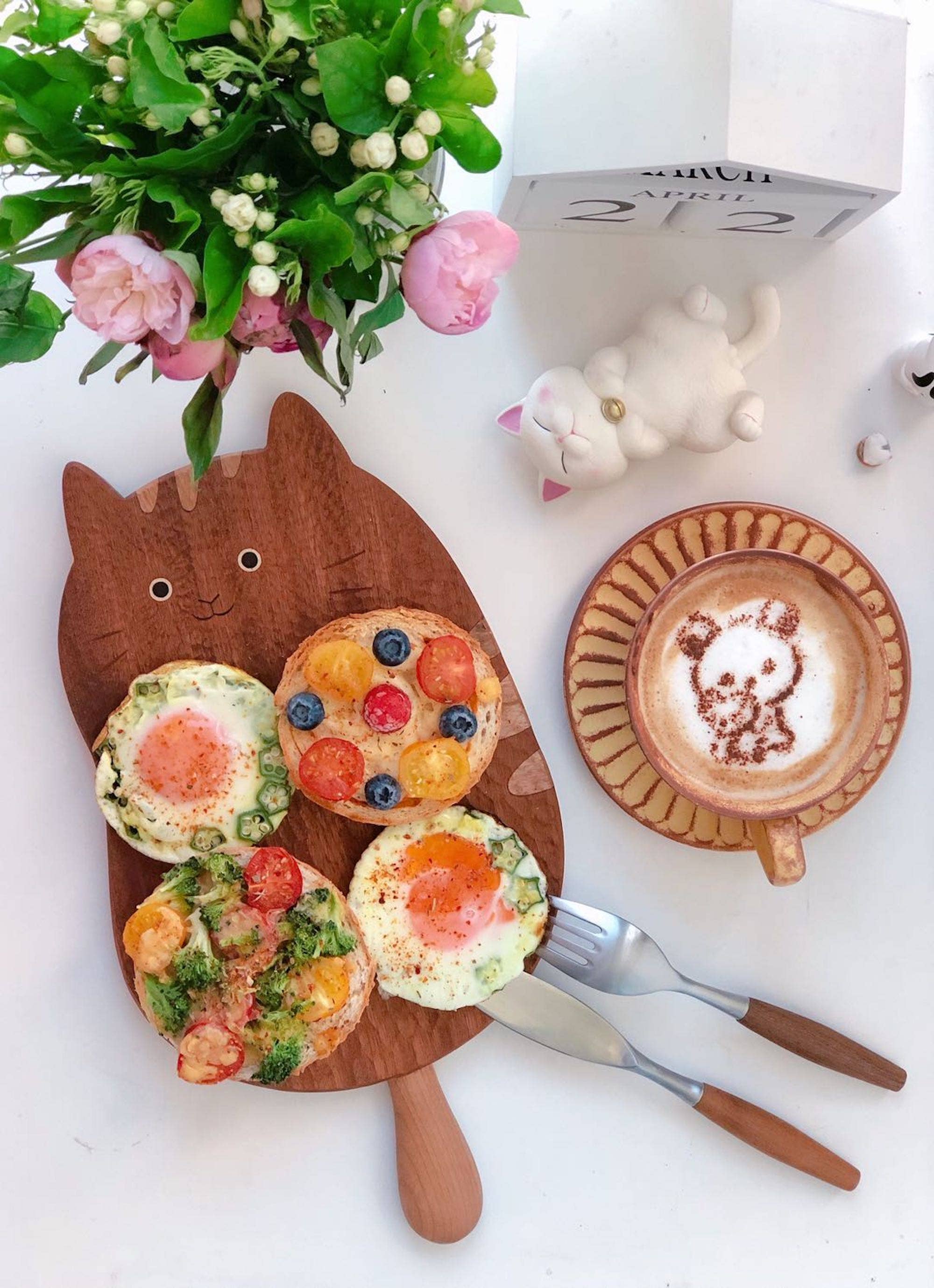 Wooden board with decorative eggs, latte art, and floral arrangement on a white surface.