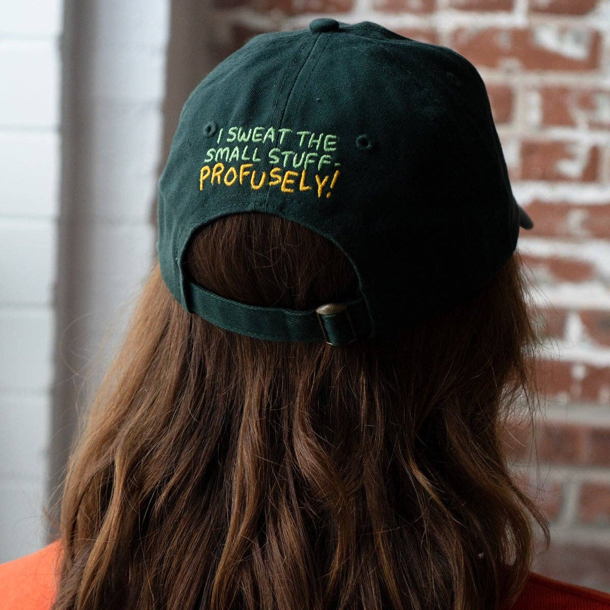 Person wearing a green cap with text, standing against a brick wall.