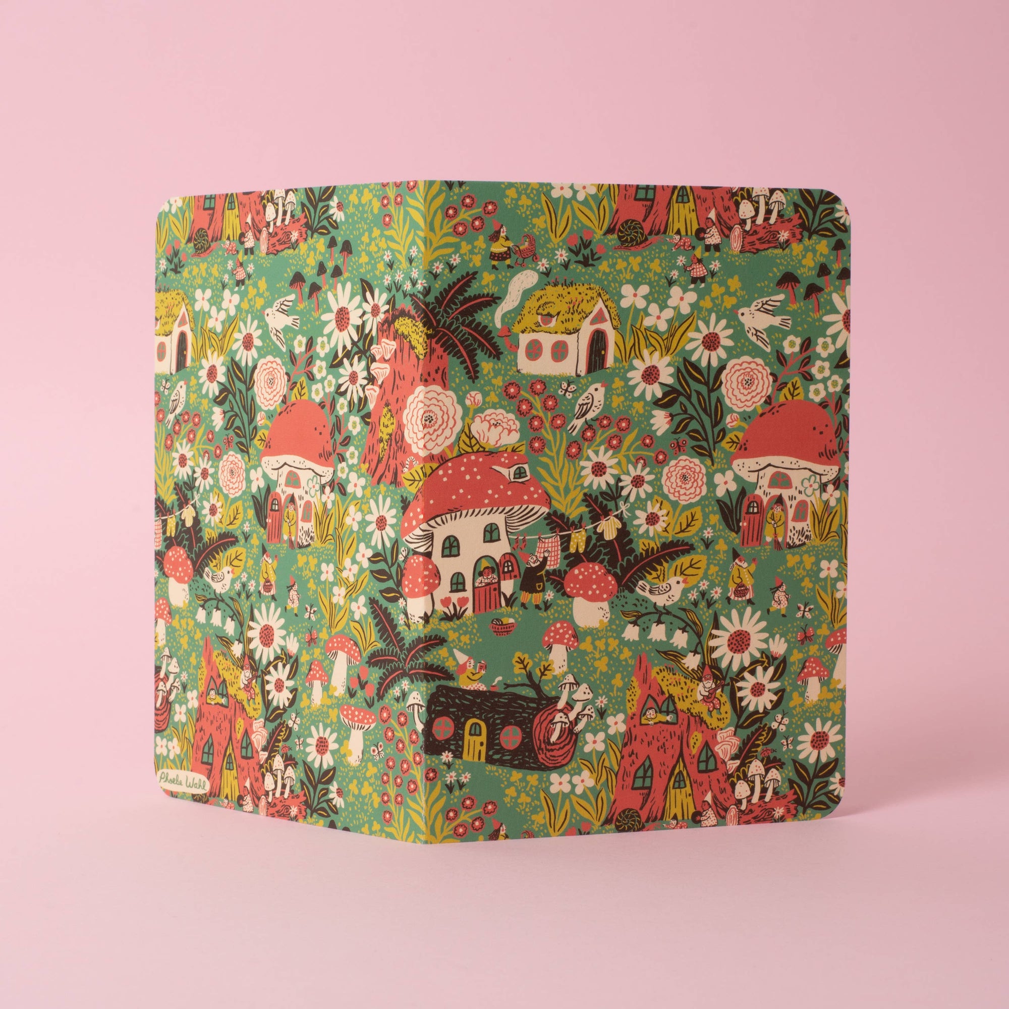 A square binder with a whimsical, colorful woodland pattern featuring mushrooms, flowers, and houses on a green background, set against a solid pink backdrop.