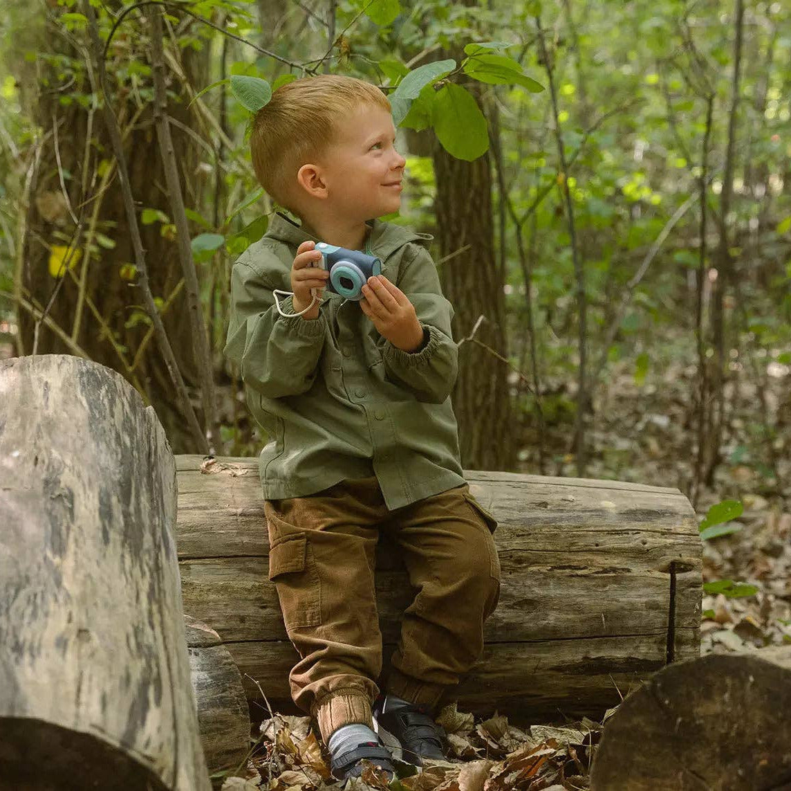 Child sitting on a log in a forest holding blue shoes