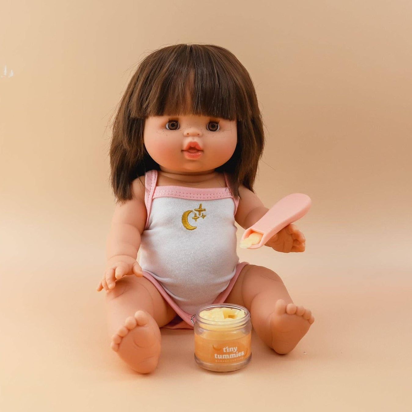 Doll with a baby outfit and toy on a beige background