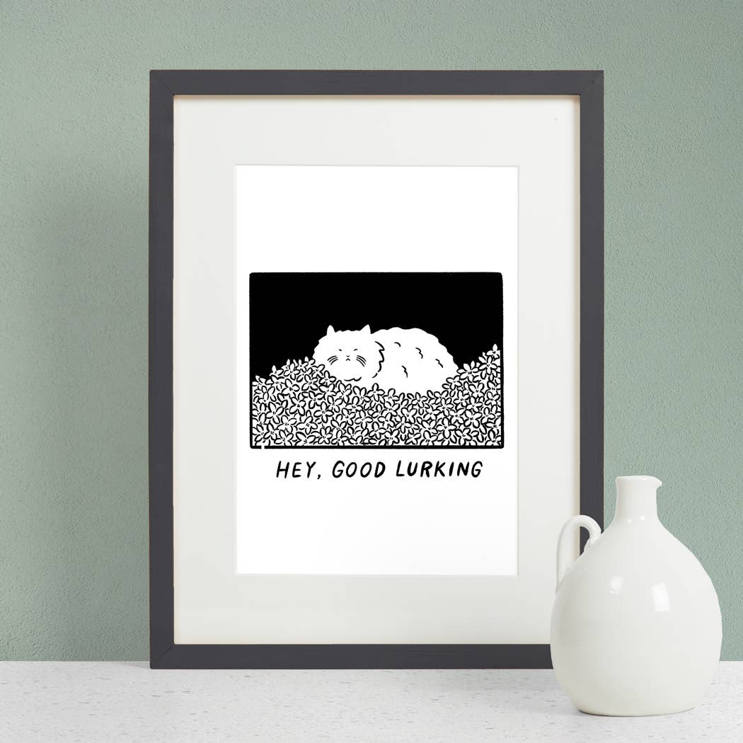 Framed artwork with a black and white illustration of a bear and text 'HEY, GOOD LURKING' on a light green wall.