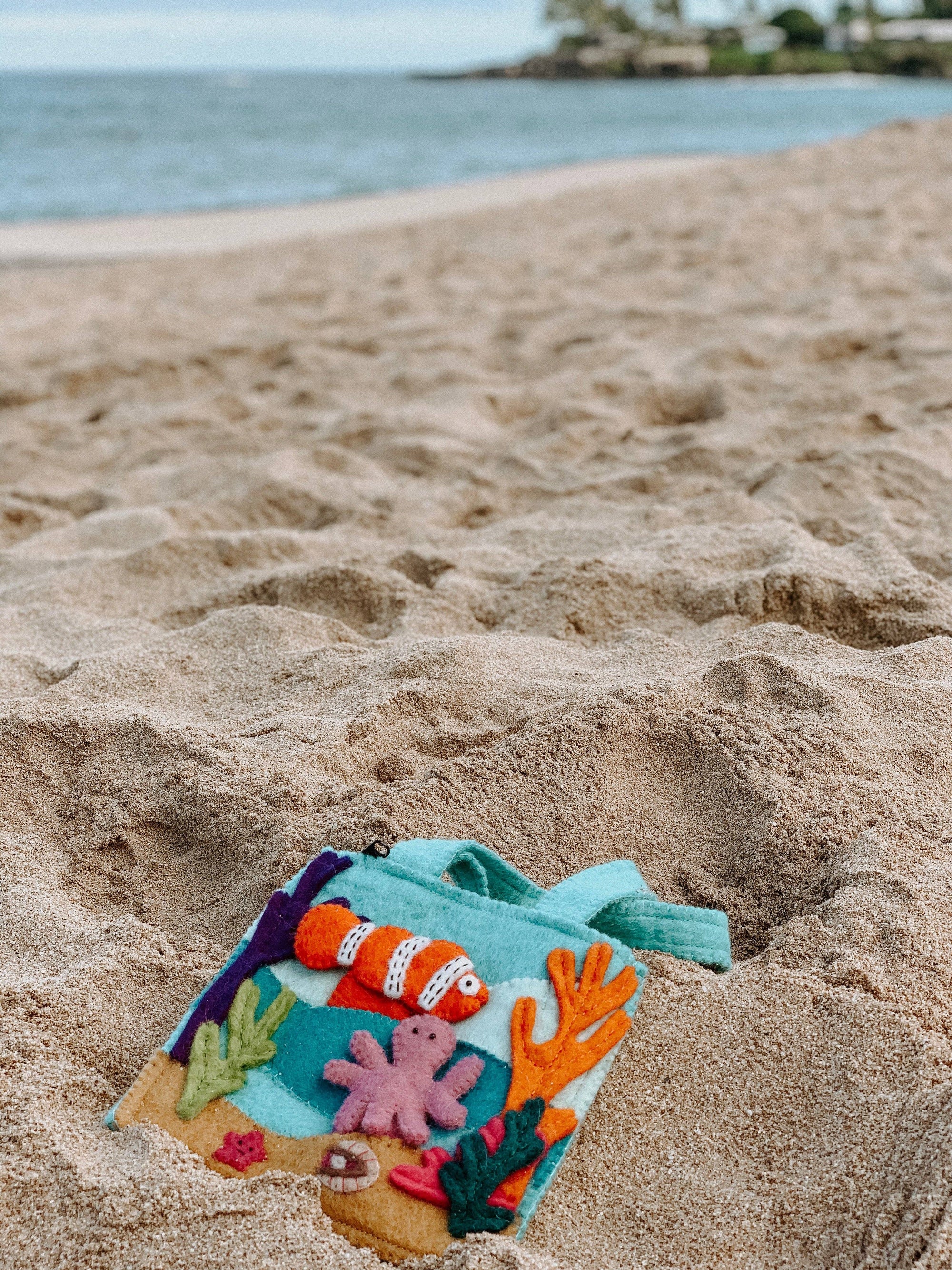Colorful children's sand toy shaped like a fish on a sandy beach with water in the background