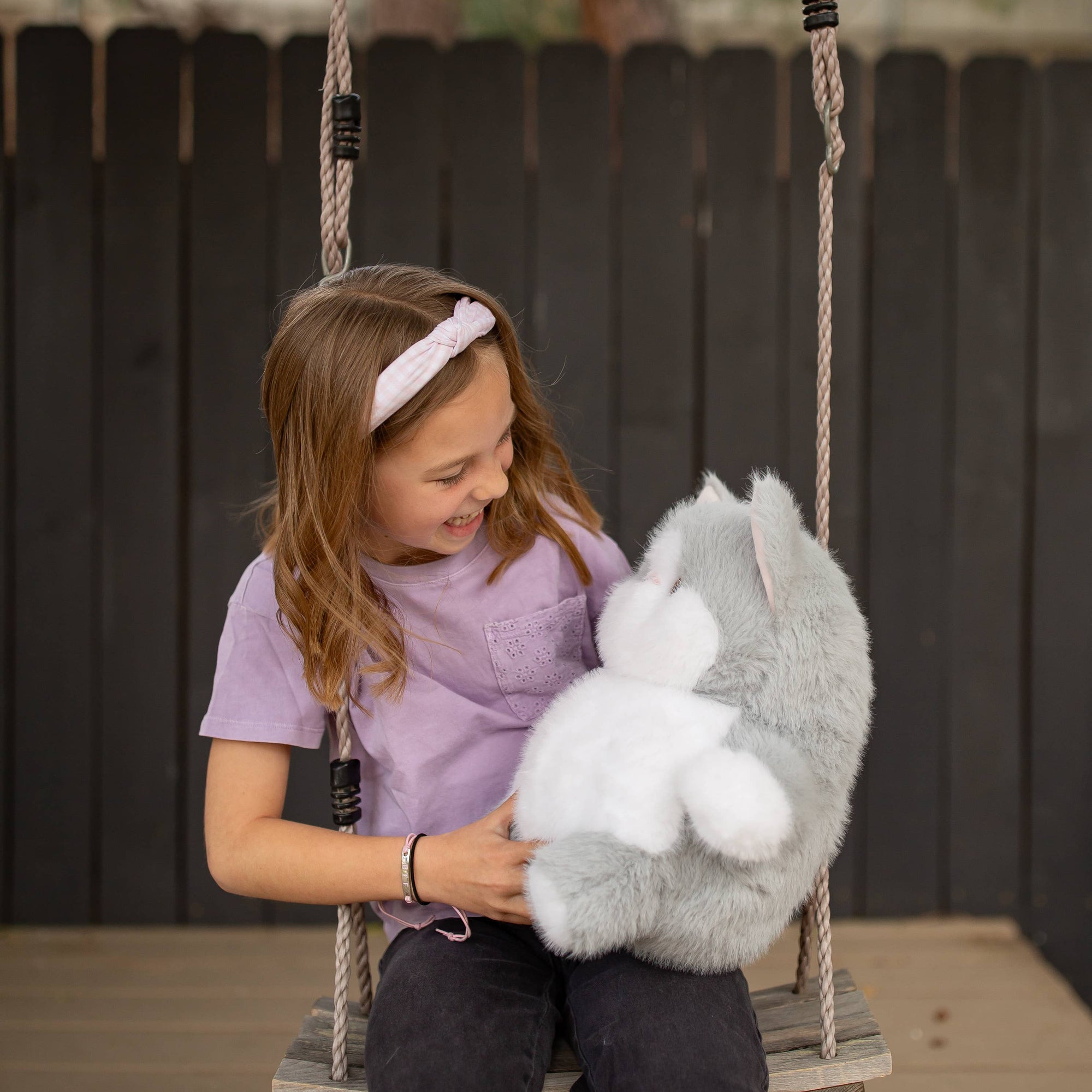 Child holding a plush toy on a swing set with a blurred background