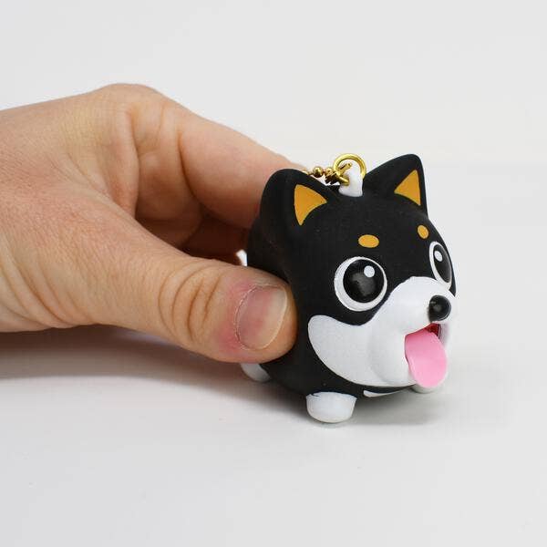 Hand holding a black and white dog-shaped keychain with a pink tongue on a light gray background
