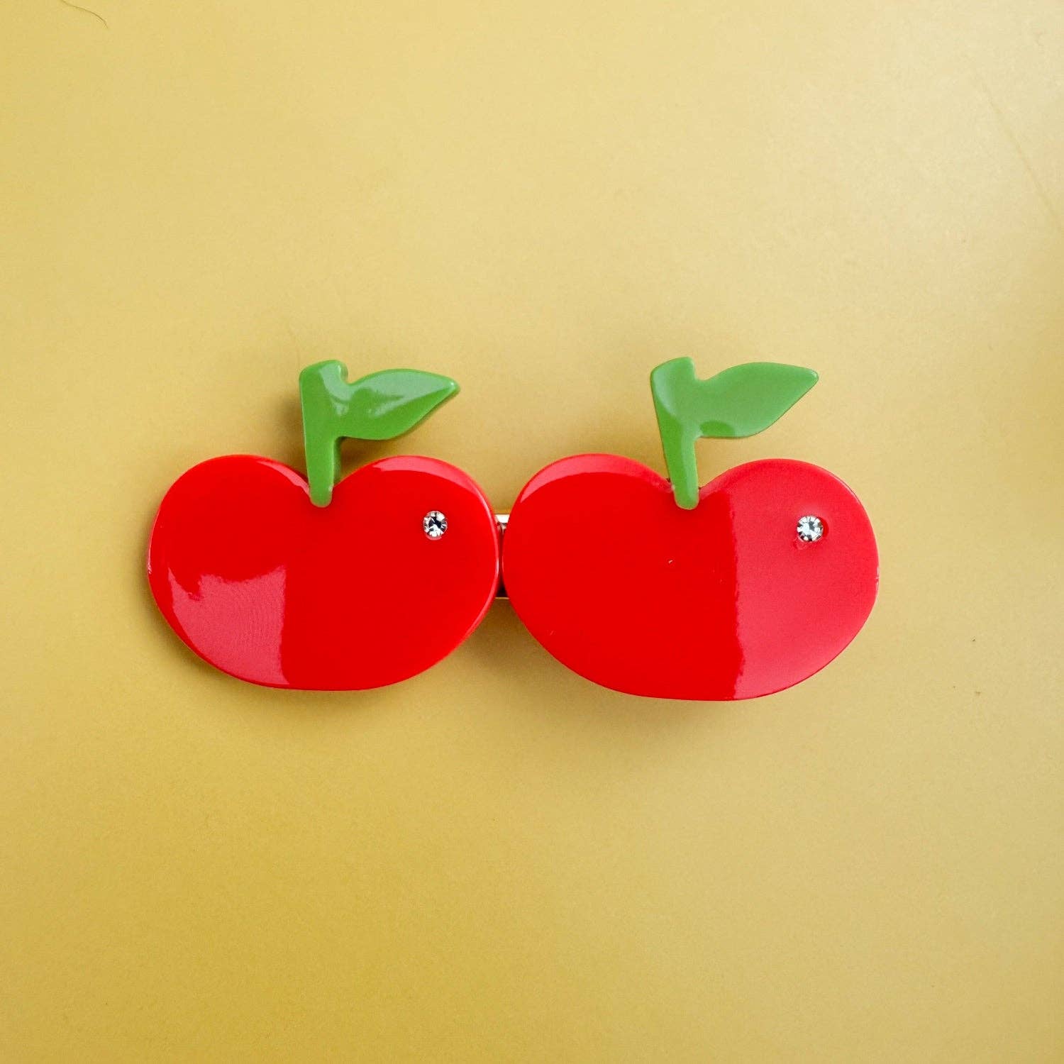 Red apple-shaped clip with green stems on a yellow background