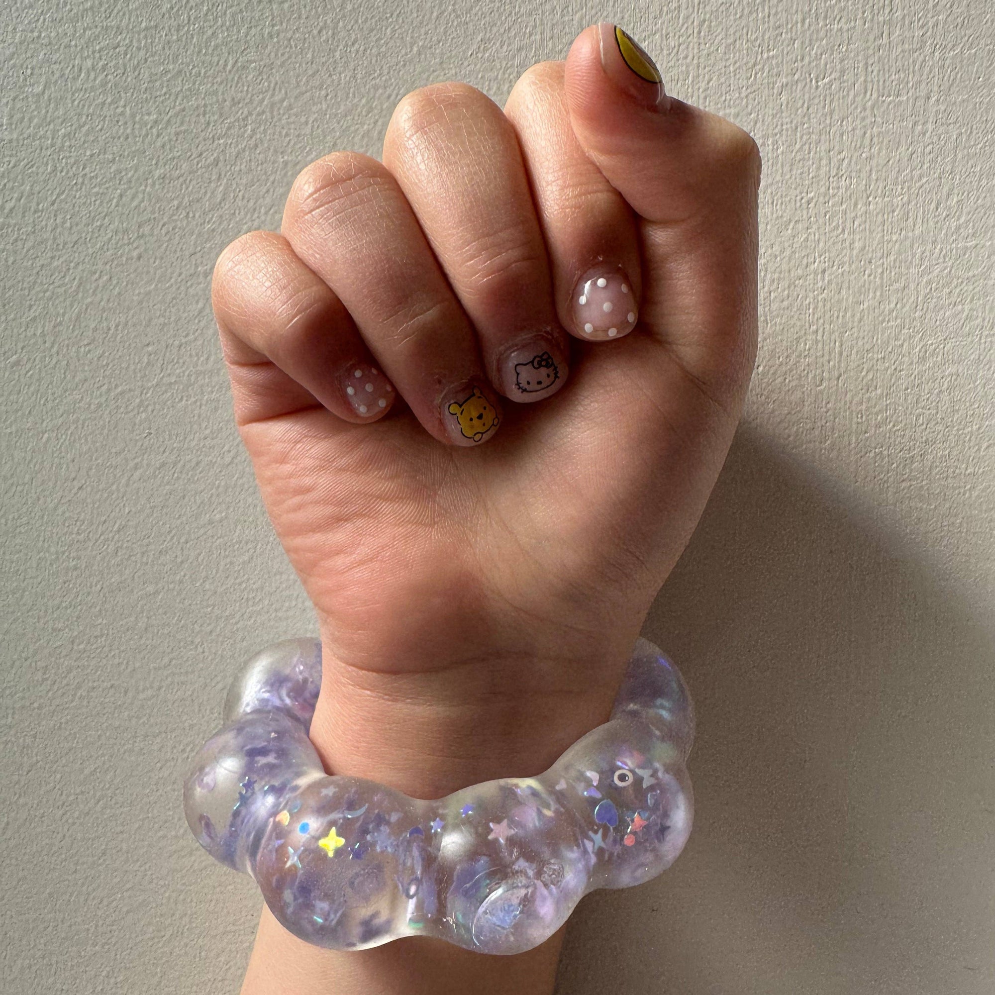 Hand wearing a glittery purple bracelet against a plain background