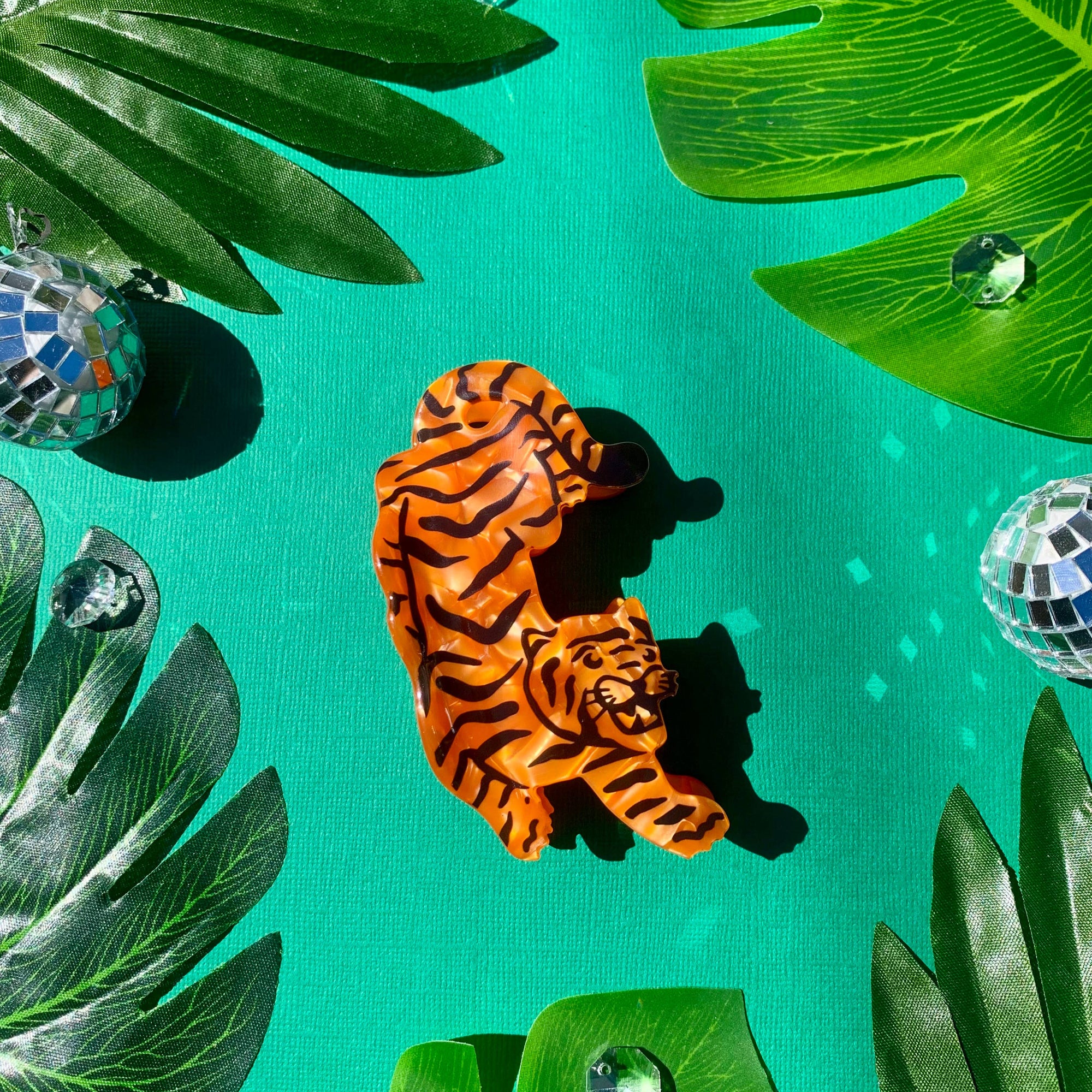 Tiger-shaped object on a green background with palm leaves and disco balls