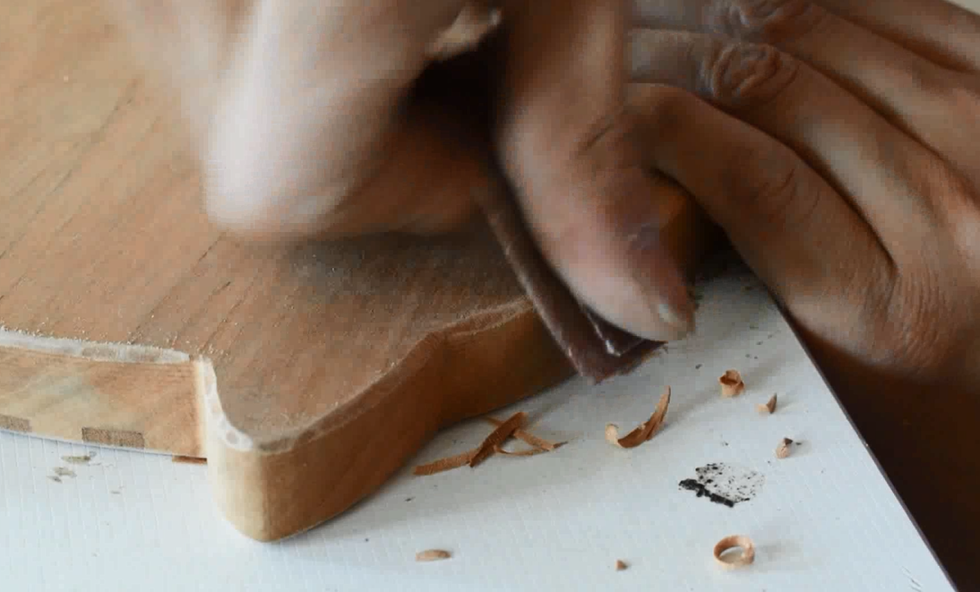 Person using a wooden tool on a white surface with small pieces of wood debris.