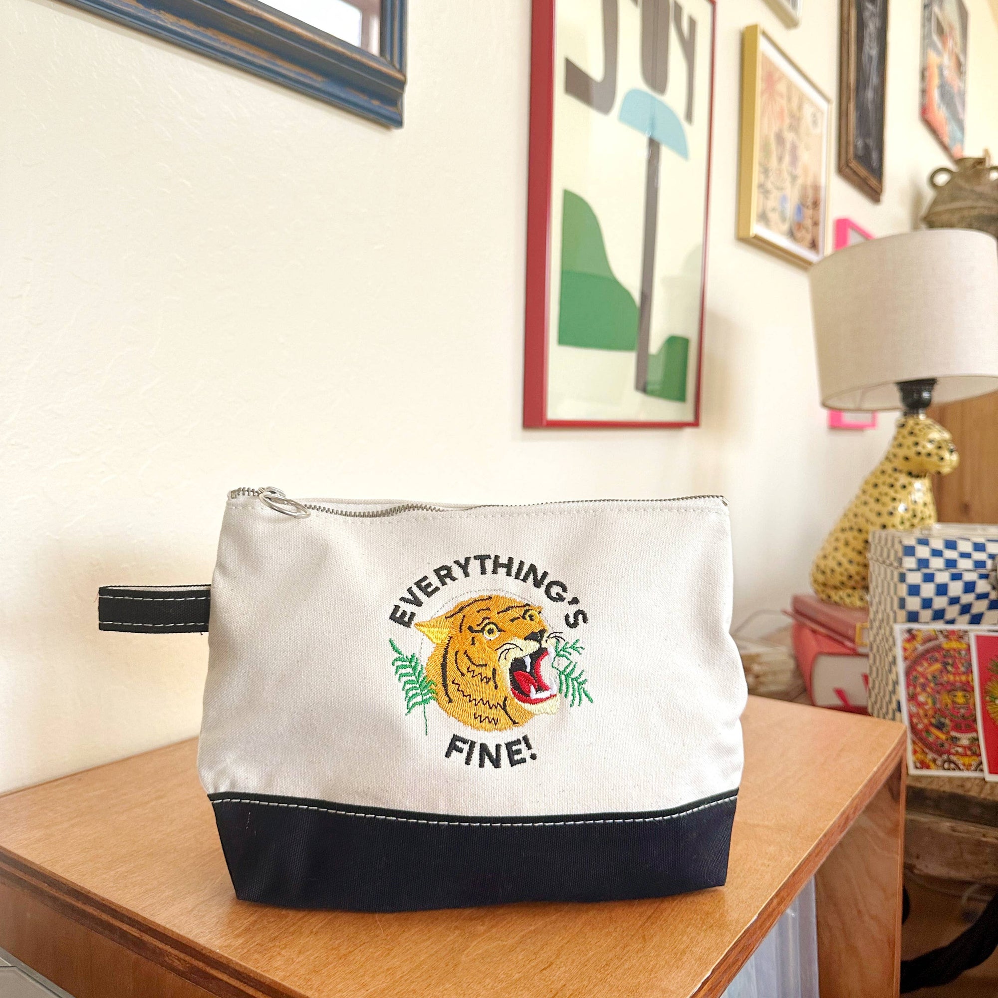White pouch with tiger graphic and 'Everything's Fine!' text on a wooden surface.