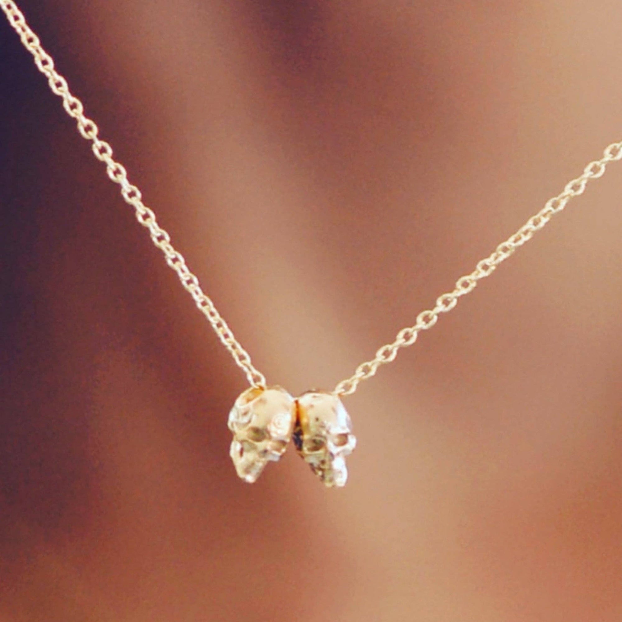 Gold necklace with a small skull like pendant against a blurred background