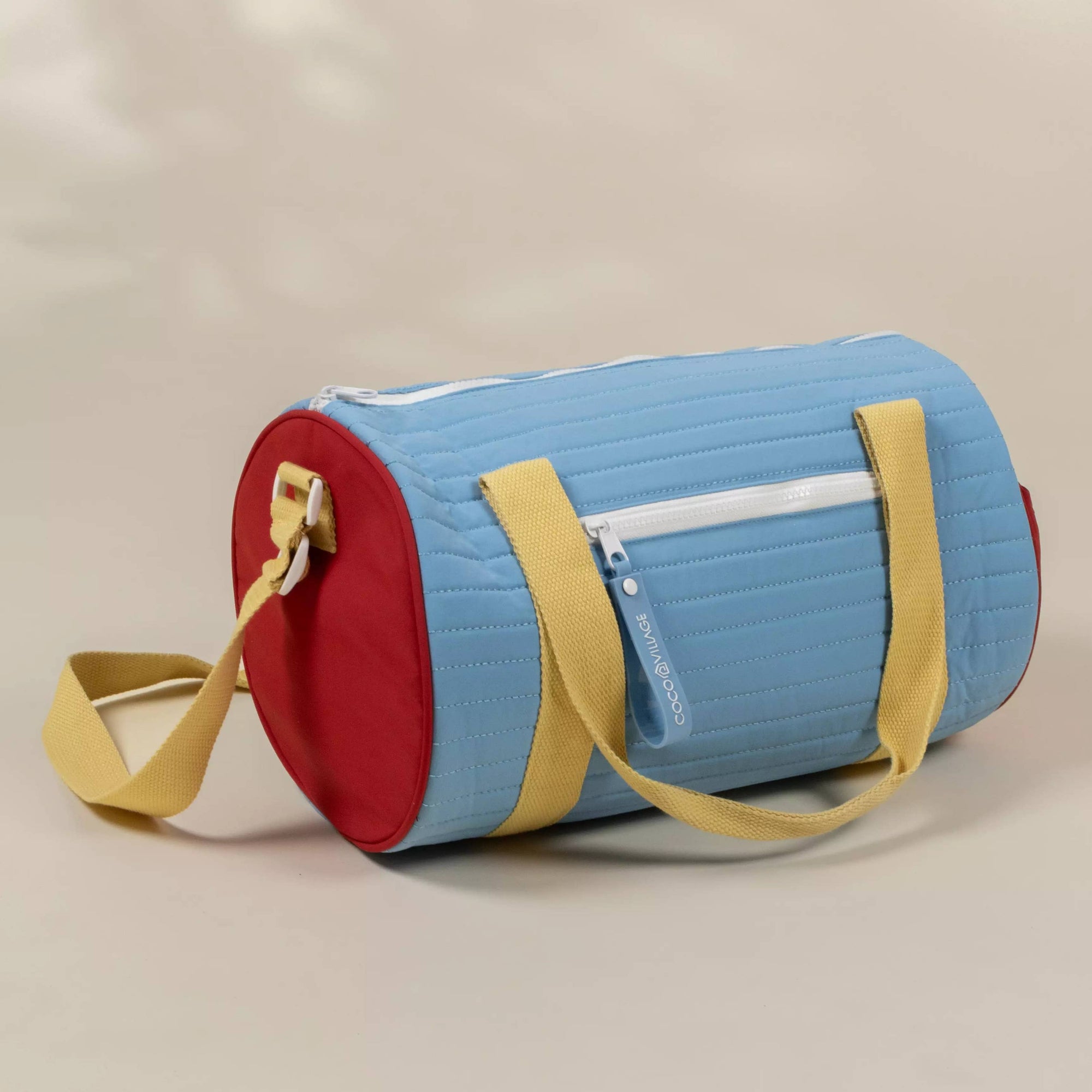 Colorful cylindrical bag with a red bottom, blue top, and yellow straps on a beige background