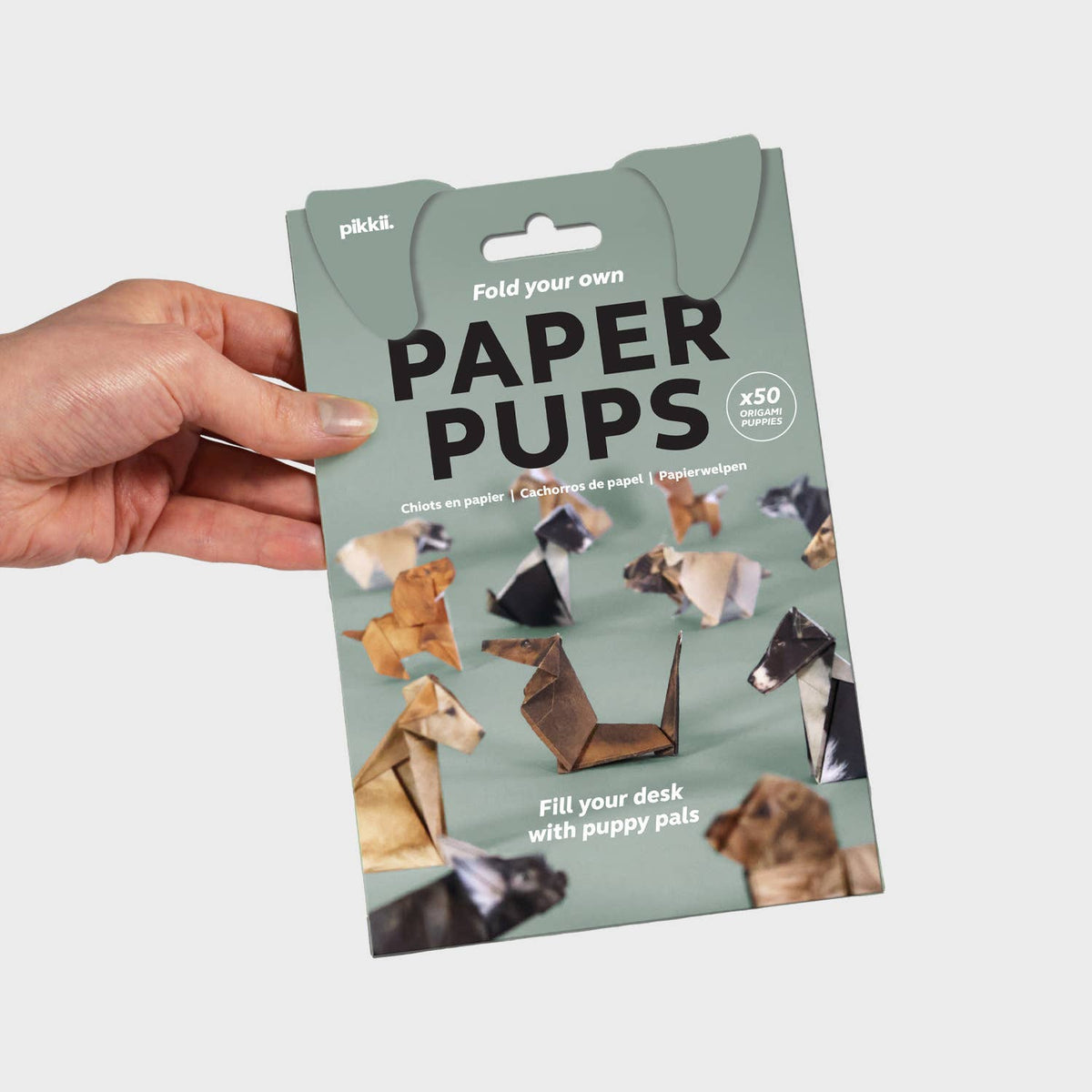 Packaging of paper puppets held by a hand with a light gray background