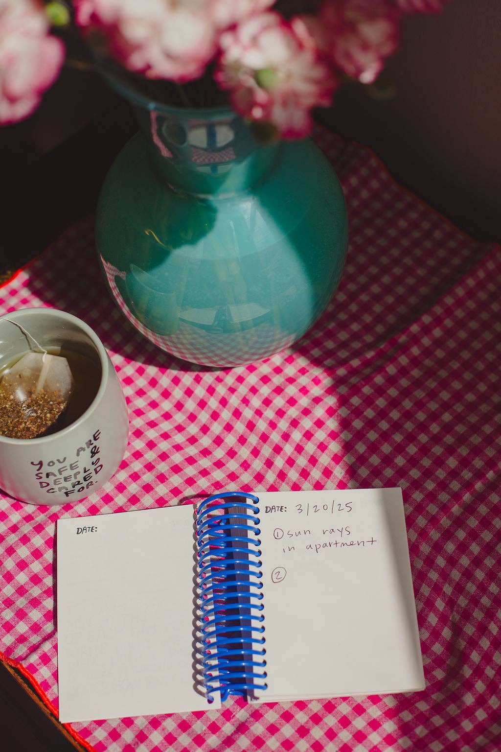 Notebook with a pen on a checkered tablecloth with a vase and flowers in the background