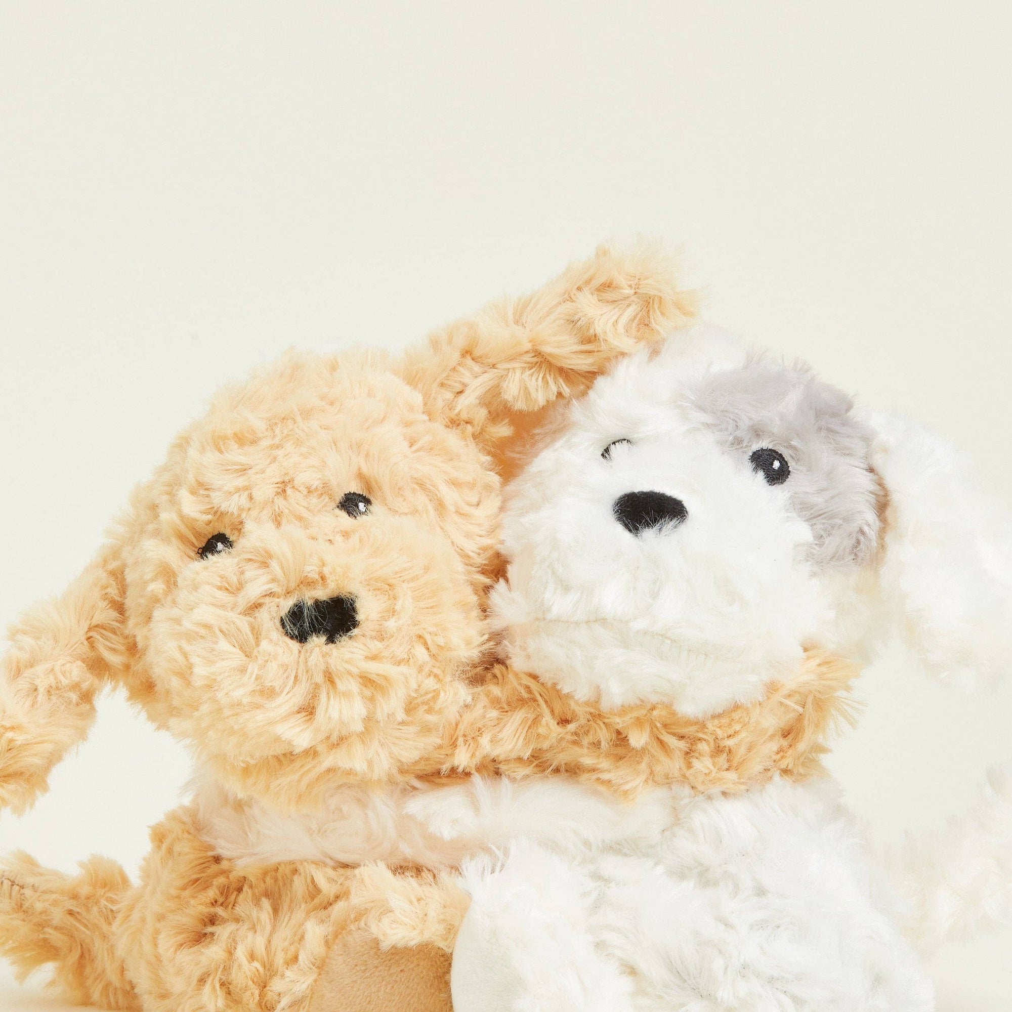 Two plush toys, one beige and one white, sitting together on a light background.