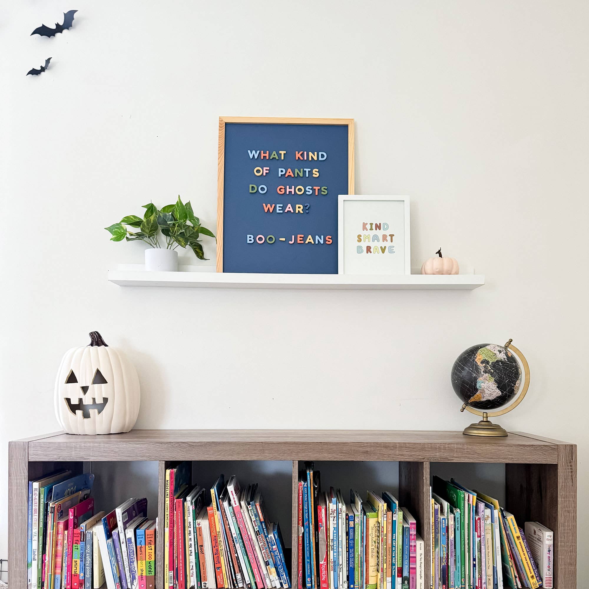 Bookshelf with Halloween decorations, books, and a framed quote on a white wall.