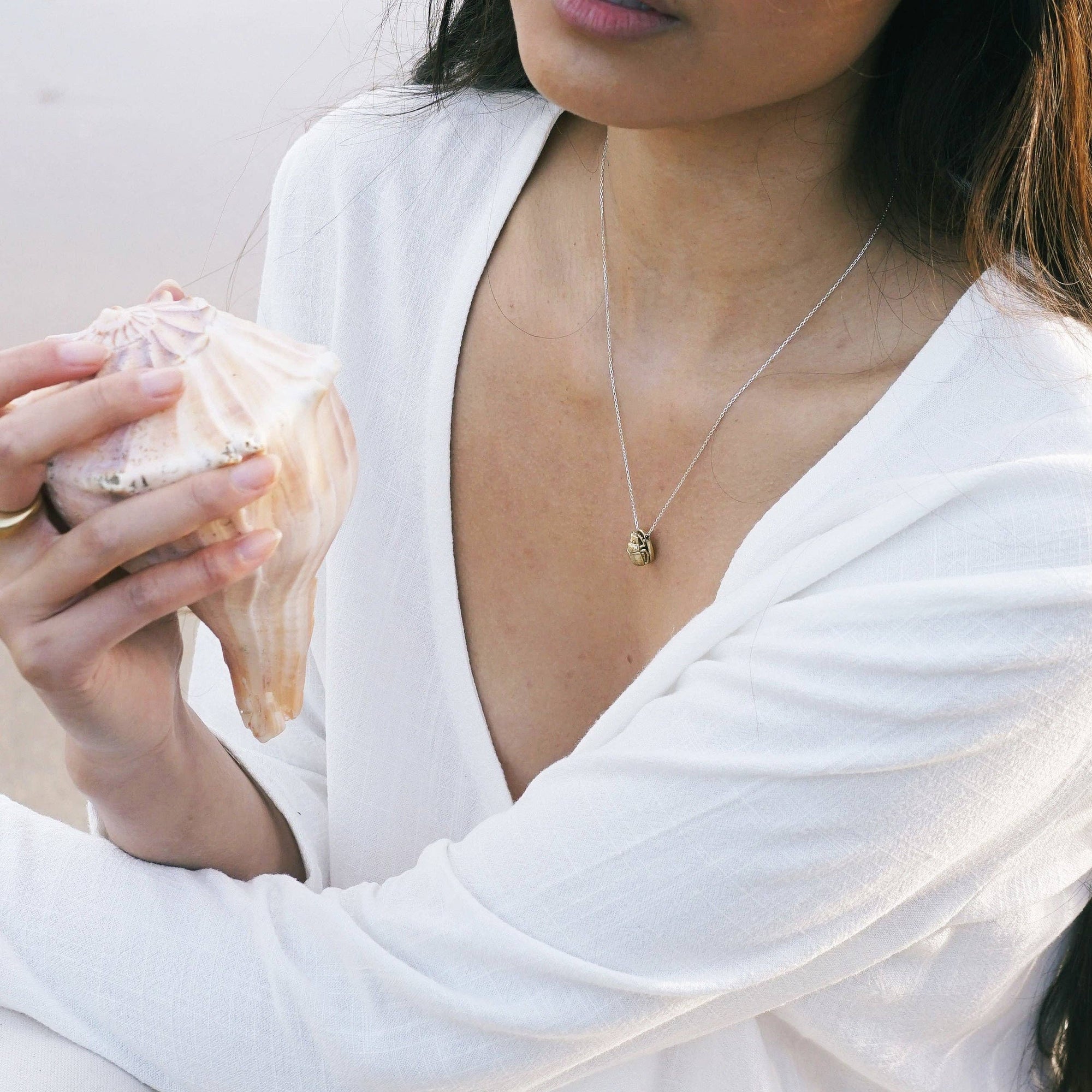 Woman in a white outfit holding a shell on a beach
