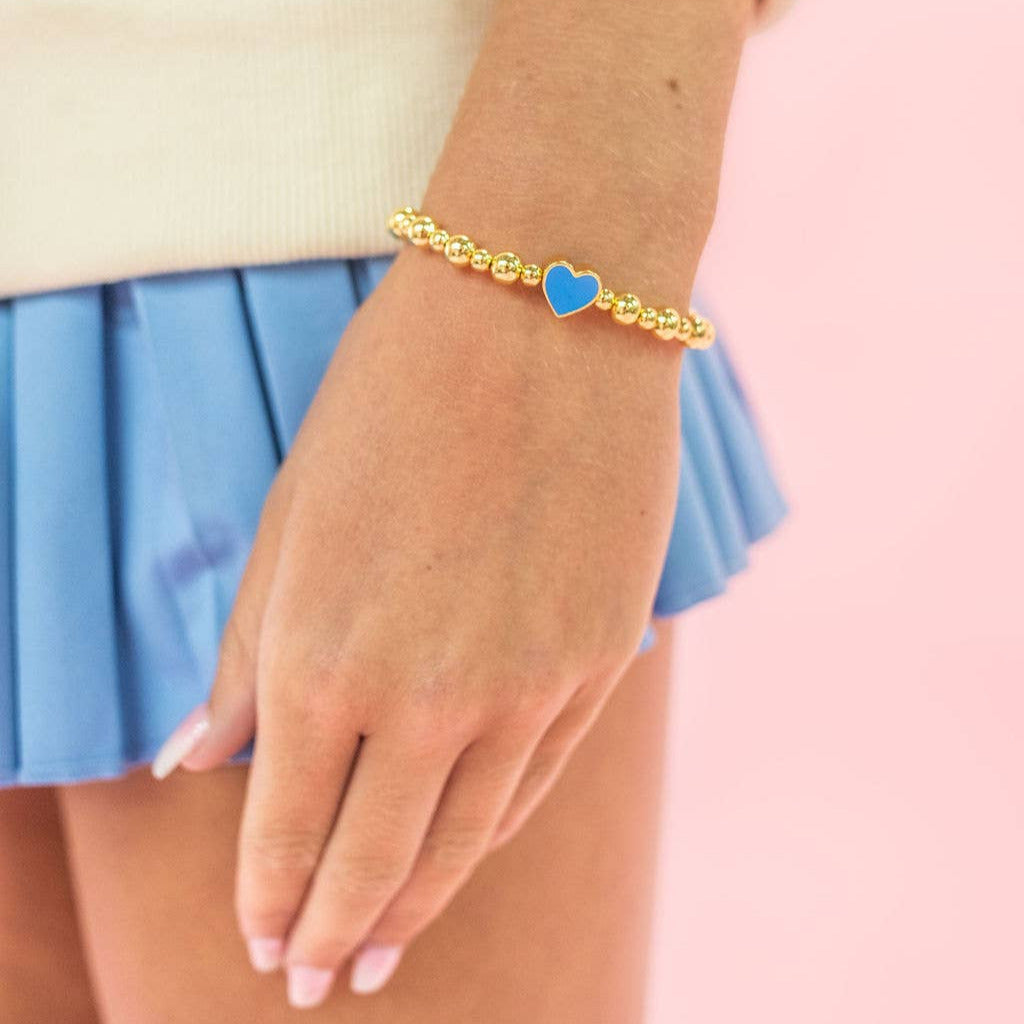 Hand wearing a bracelet with a blue heart charm on a pink background