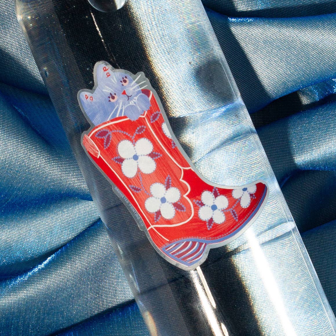 Decorative sticker with red boot and floral design on a blue fabric background