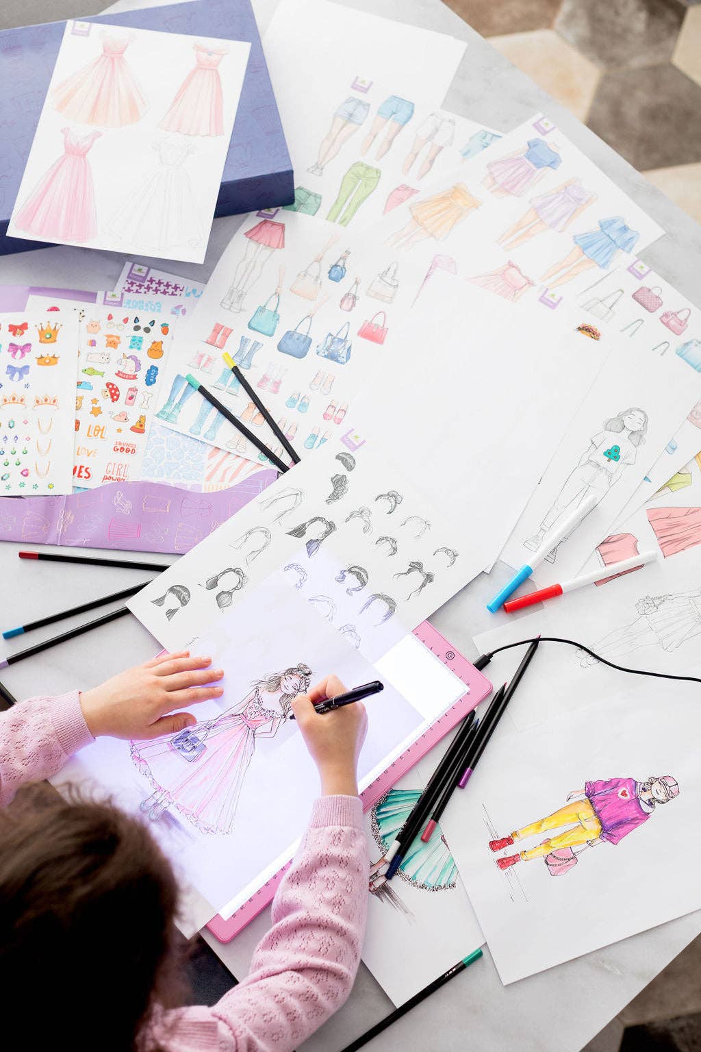 Child drawing with coloring books and markers on a table.
