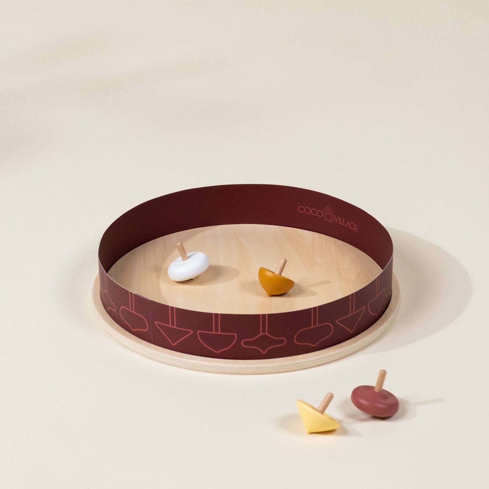 Wooden spinning tops on a circular tray with a maroon rim on a beige background