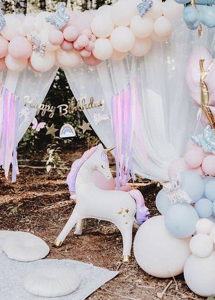 Decorative arch with balloons and a unicorn statue at a birthday party.
