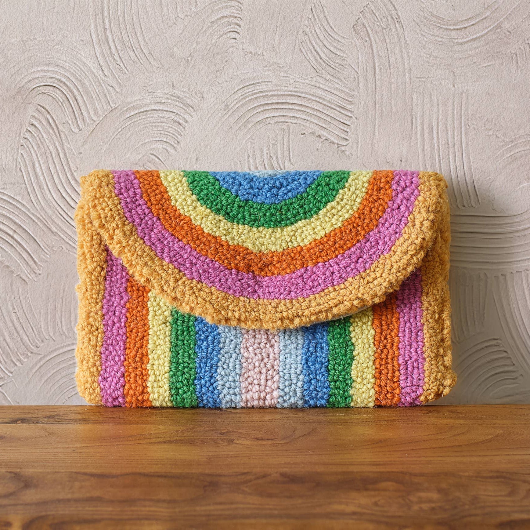 Colorful striped clutch bag on a wooden surface with a textured gray wall background
