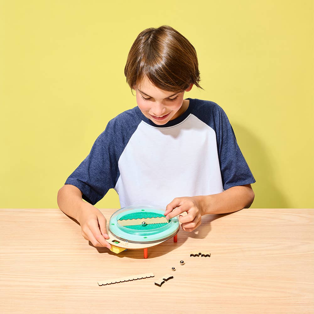 Child playing with a green toy on a wooden table against a yellow background