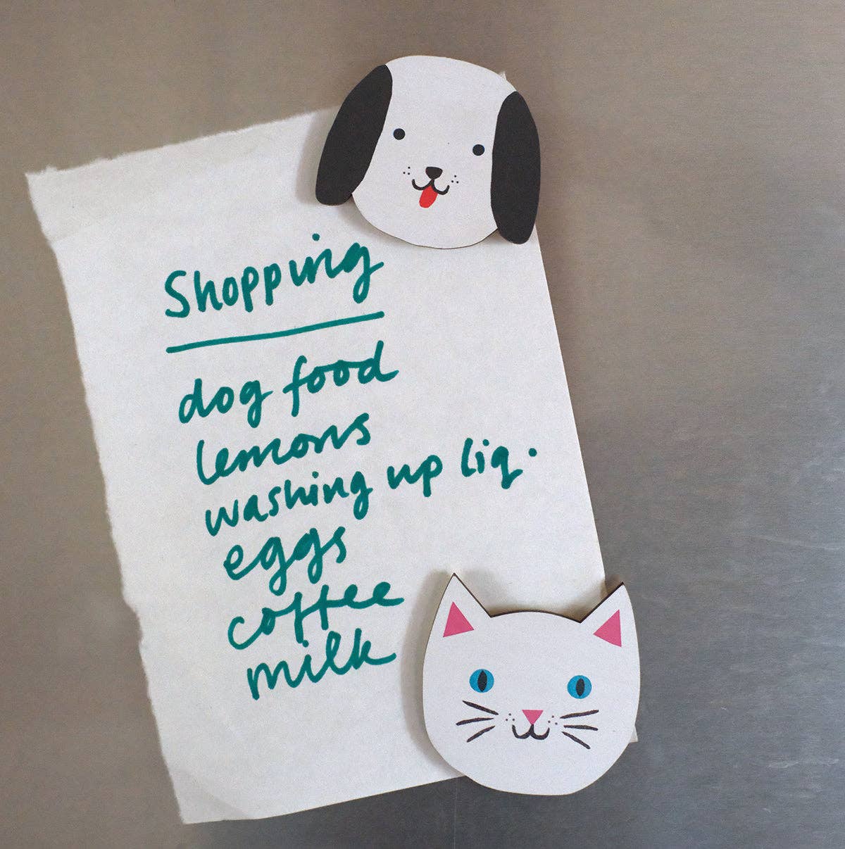 White paper with shopping list attached to a refrigerator with dog and cat-shaped magnets.