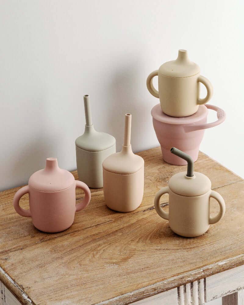 Collection of silicone cups and straws on a wooden surface with a white wall background