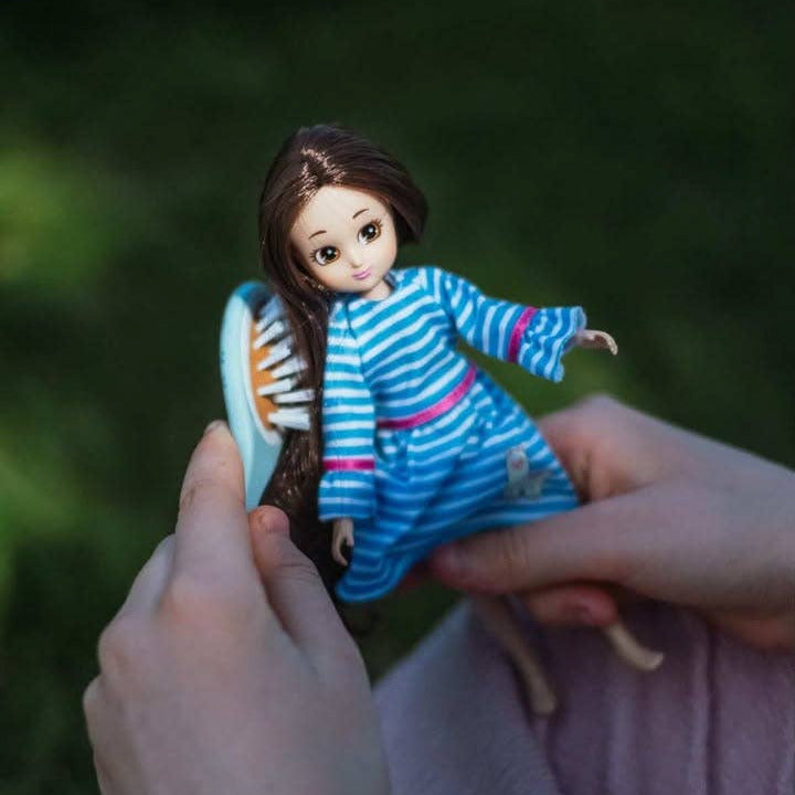 Person holding a small doll with a blue striped dress against a blurred green background
