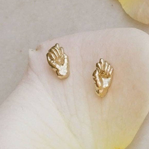 Gold hand-shaped earrings on a white petal