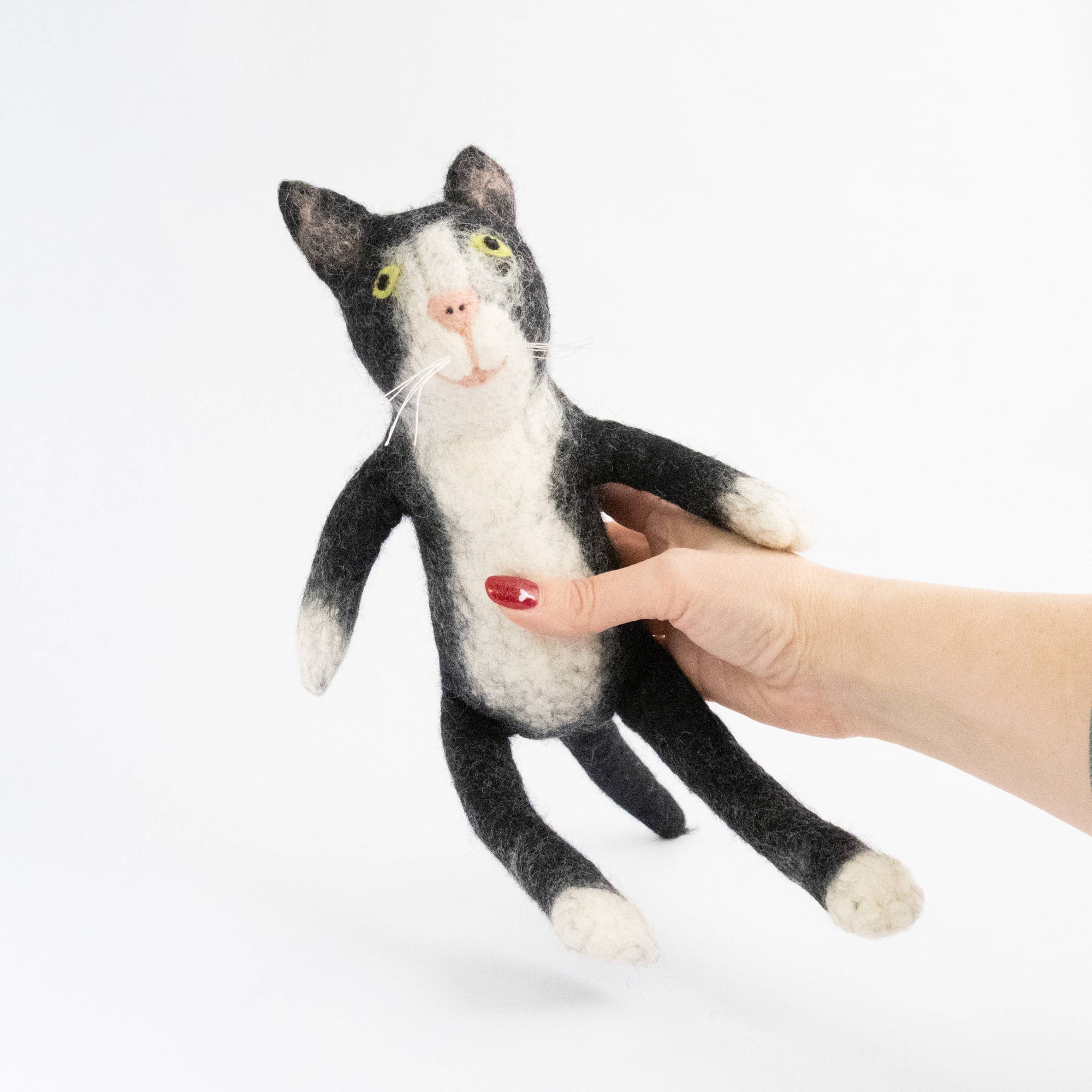 Hand holding a black and white cat-shaped plush toy on a white background