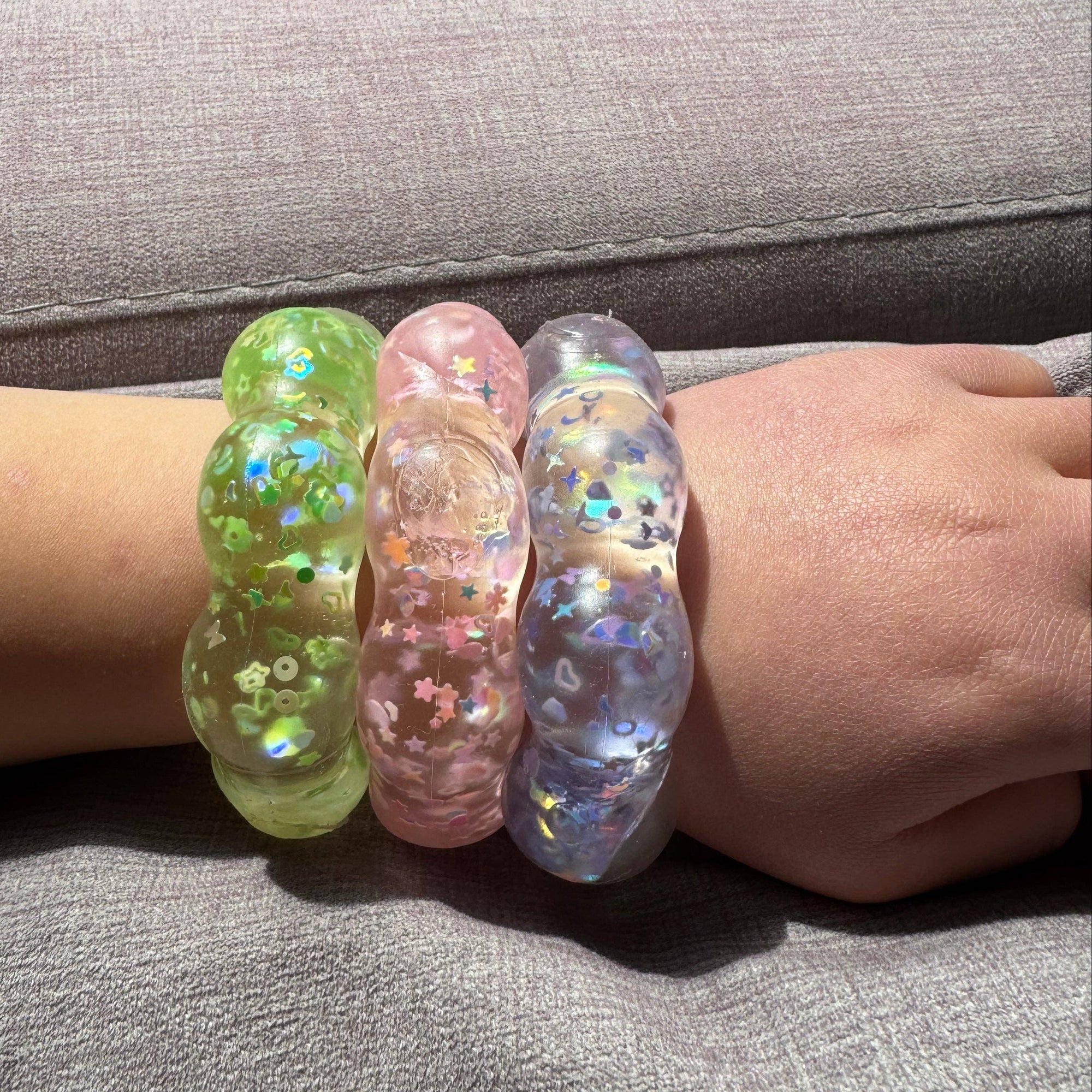 Three colorful bracelets on a person's wrist with a neutral background