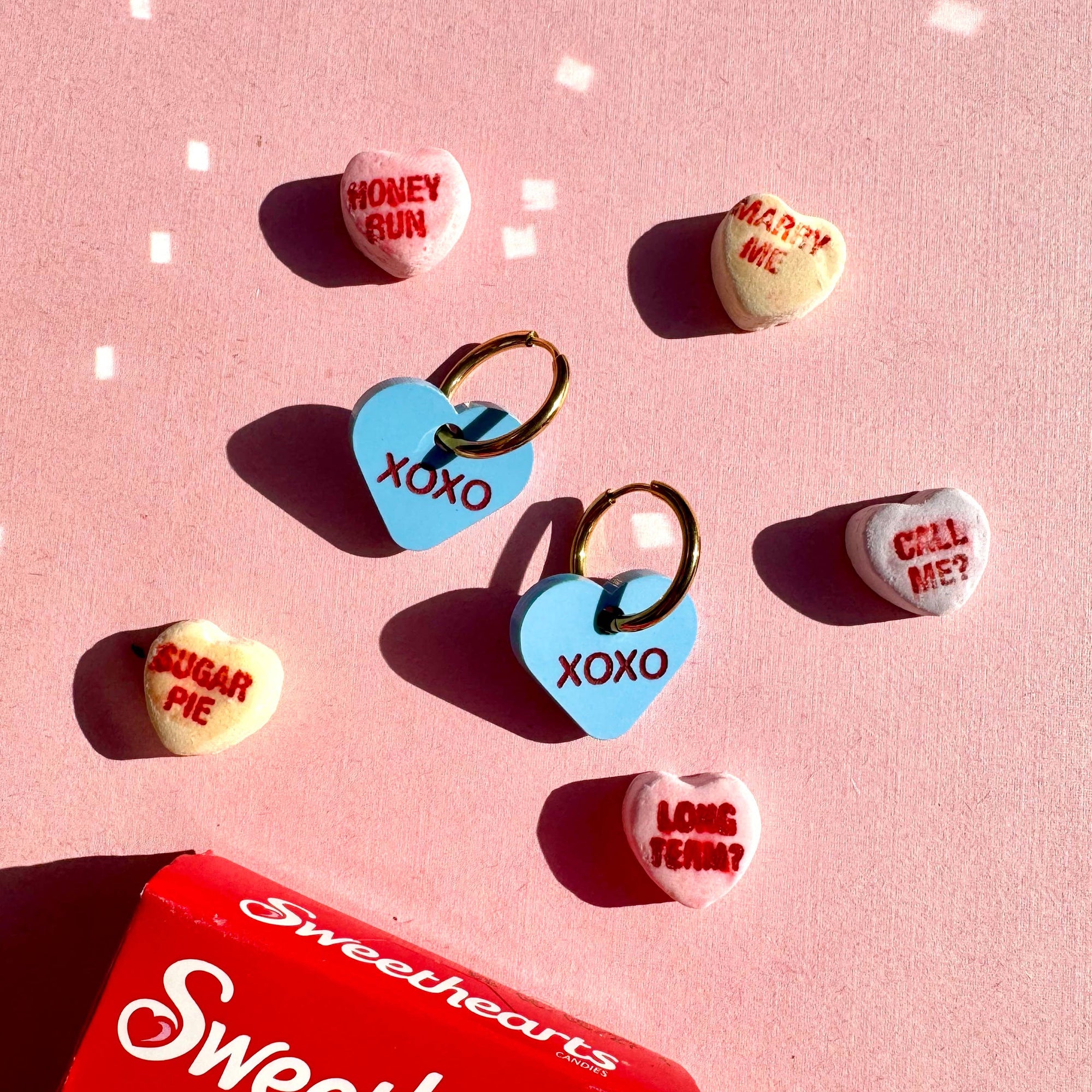 Sweethearts candy hearts with various messages on a pink background, featuring a red Sweethearts box.