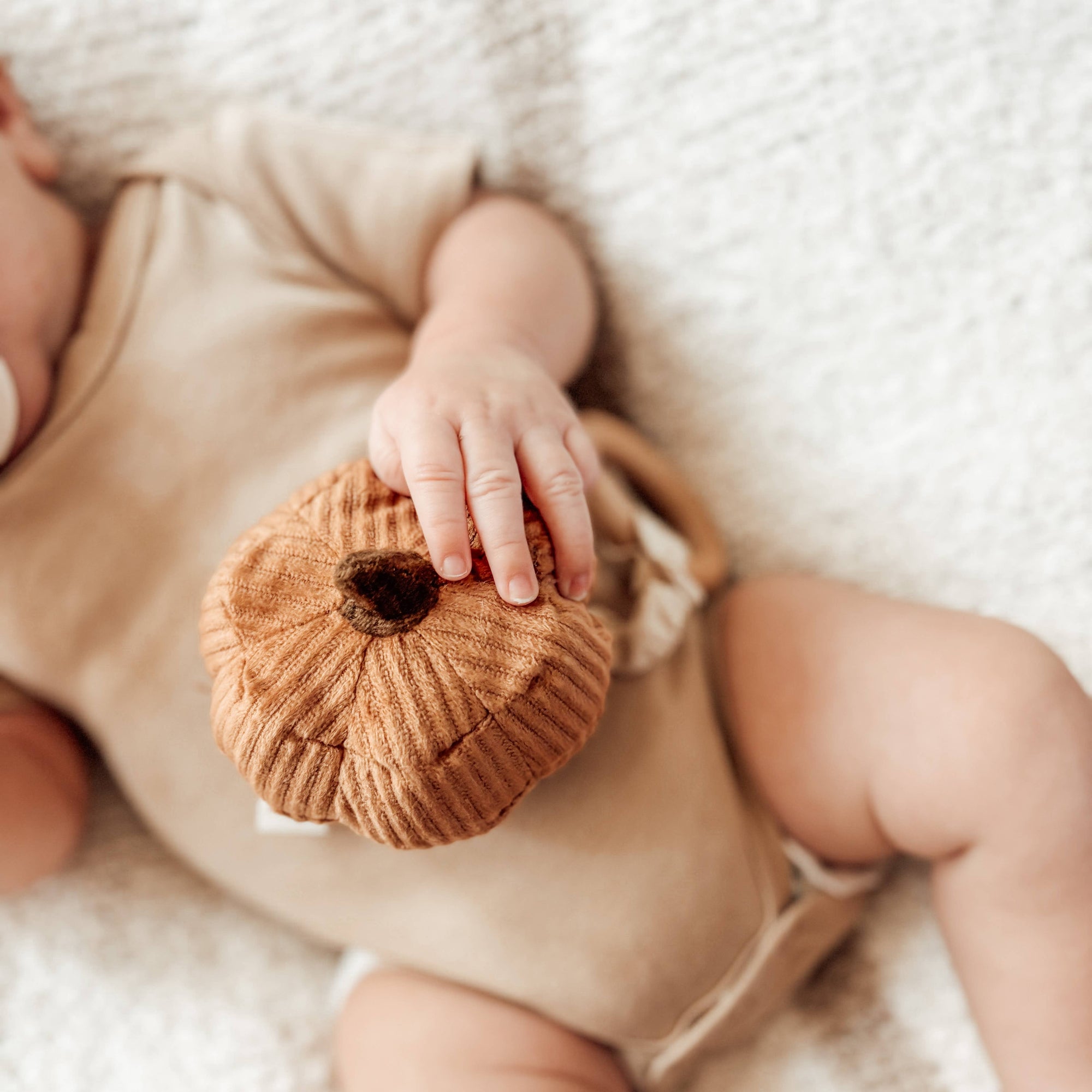 Baby holding a small brown knitted toy on a soft white background